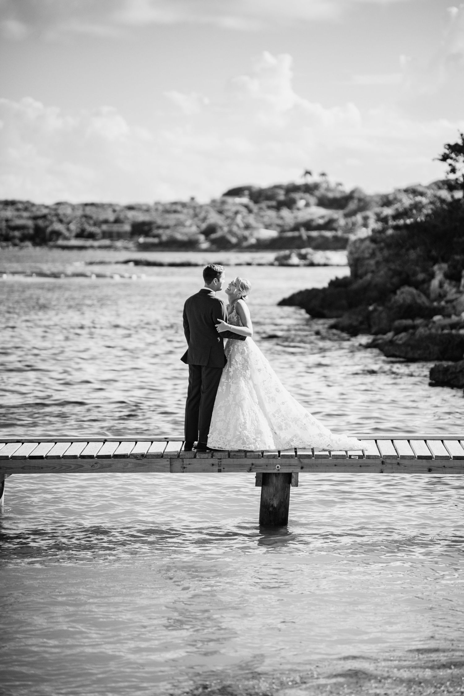 Romantic black and white photo of a couple standing on a wooden pier overlooking the ocean.