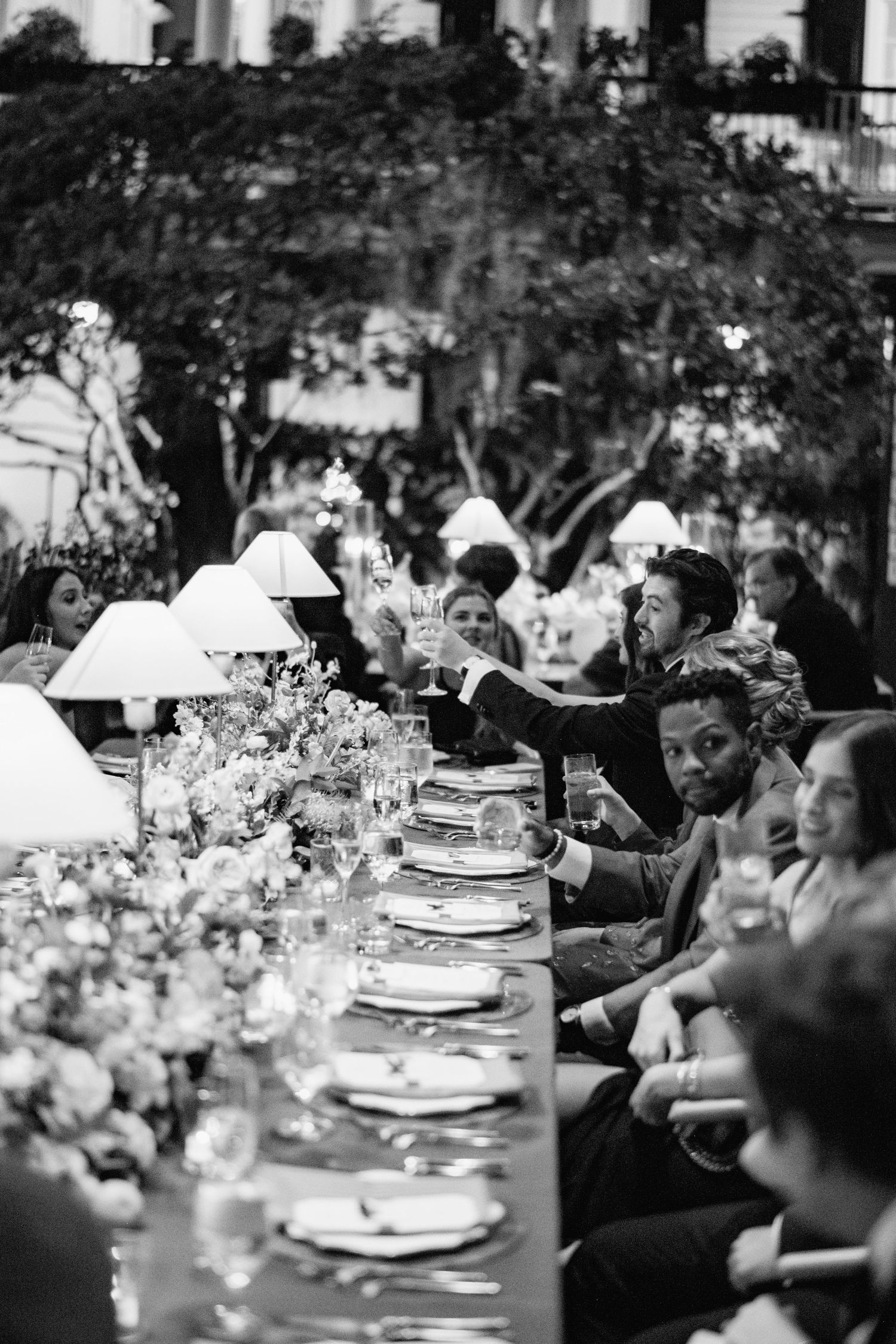 Black and white photograph of guests dining at an elegant outdoor reception with table settings and floral centerpieces.