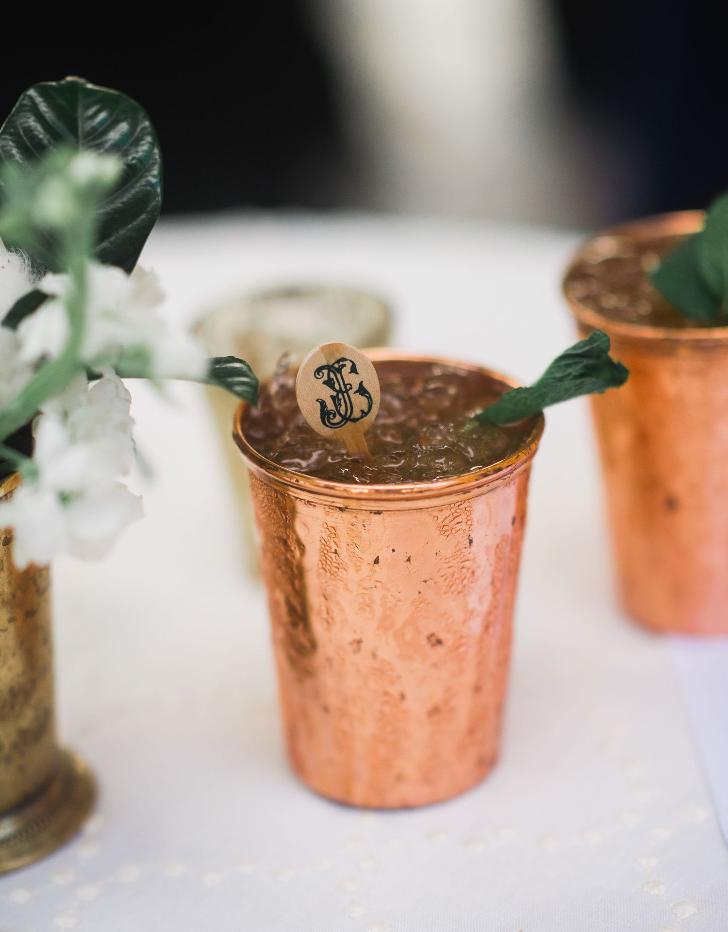 Vintage copper cocktail cups with mint garnish on white surface, styled for elegant drink service.