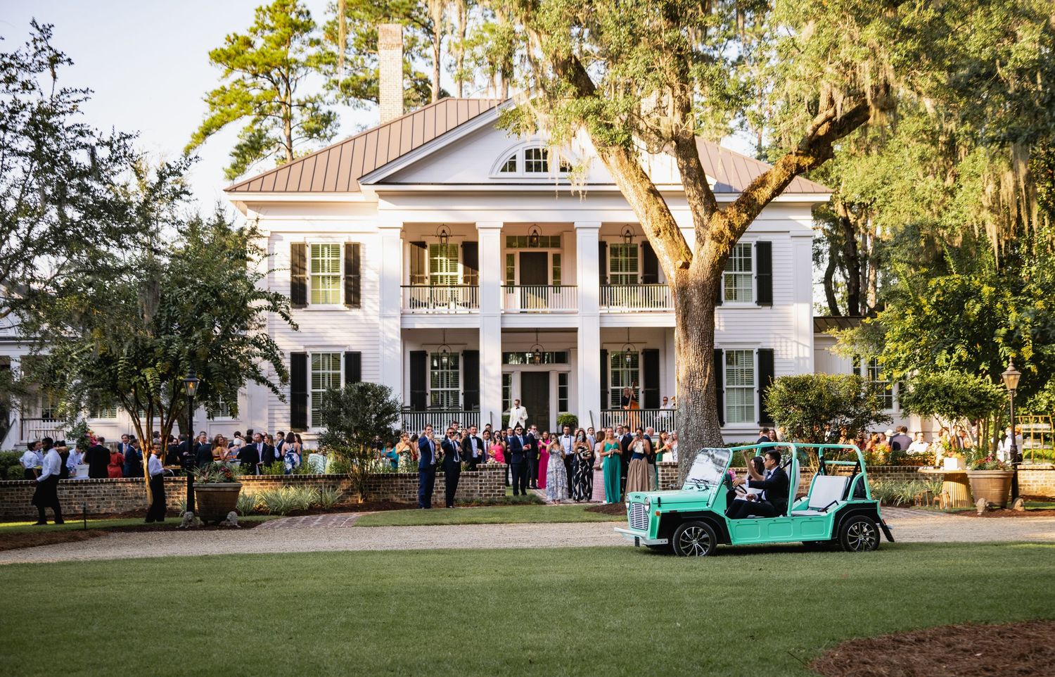 A grand white antebellum mansion with columns and a turquoise golf cart parked on the lawn during an outdoor gathering.