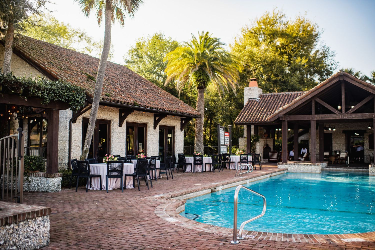 A serene resort swimming pool surrounded by palm trees and traditional wooden buildings with tiled roofs.
