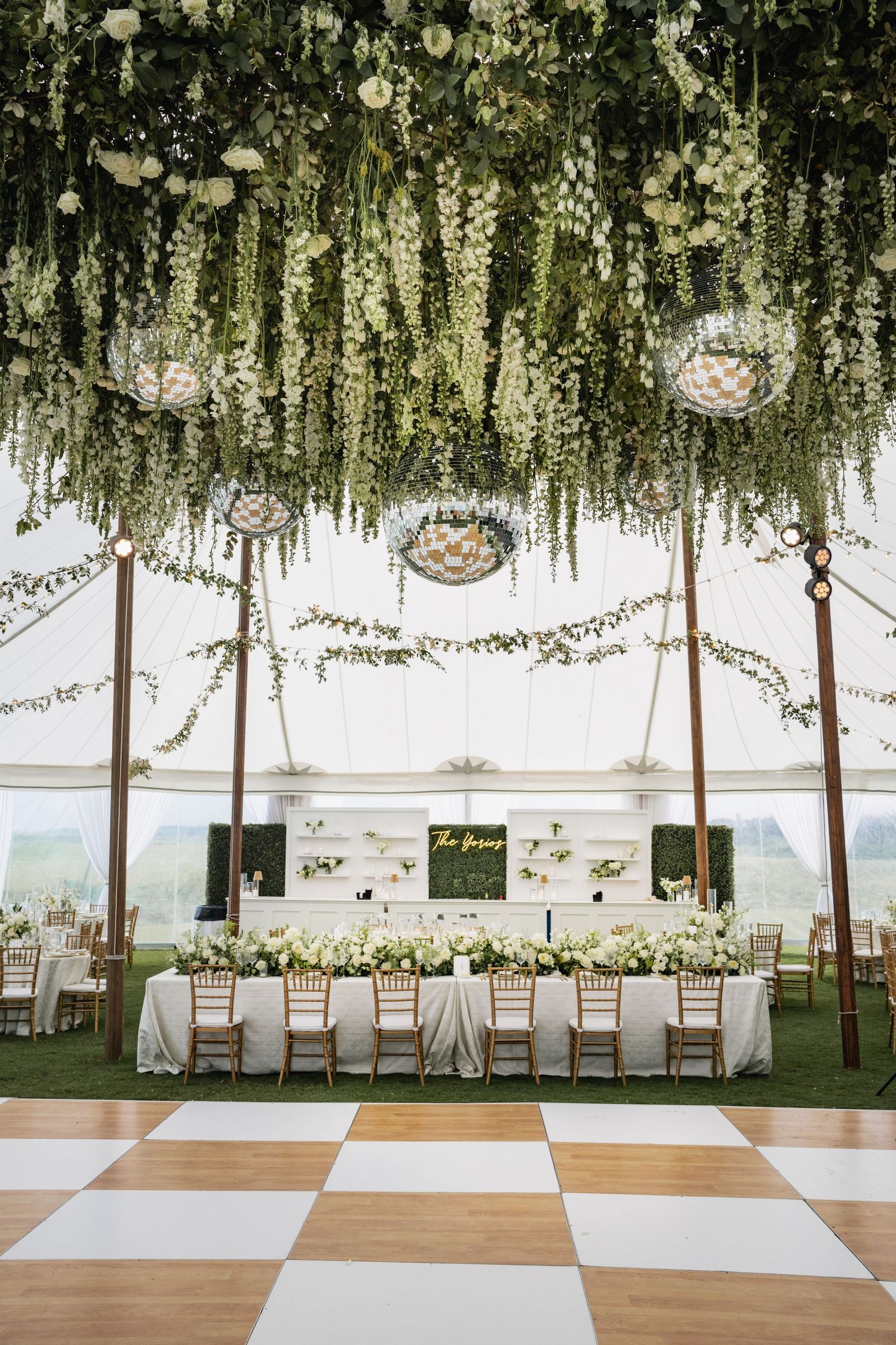Elegant wedding reception tent with hanging floral installations, chandeliers and checkered dance floor.