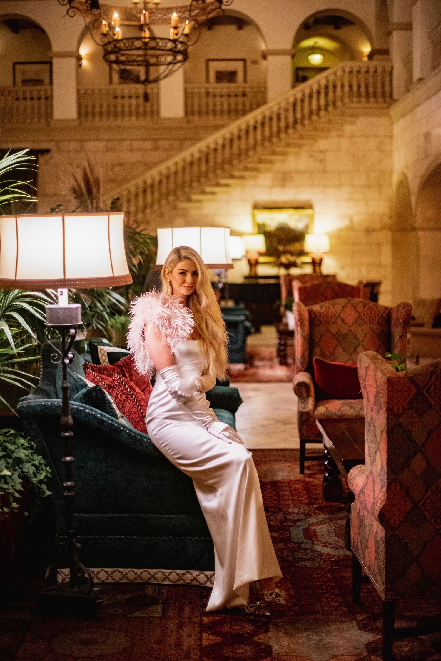 Elegant evening scene in luxurious hotel lobby with ornate staircase, warm lighting and plush red velvet furniture.