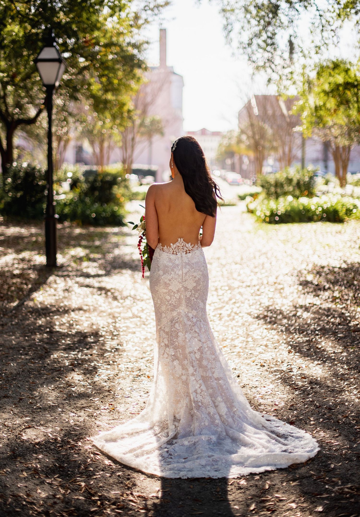A stunning lace wedding dress with intricate details captured in a sunlit outdoor setting with fallen leaves.