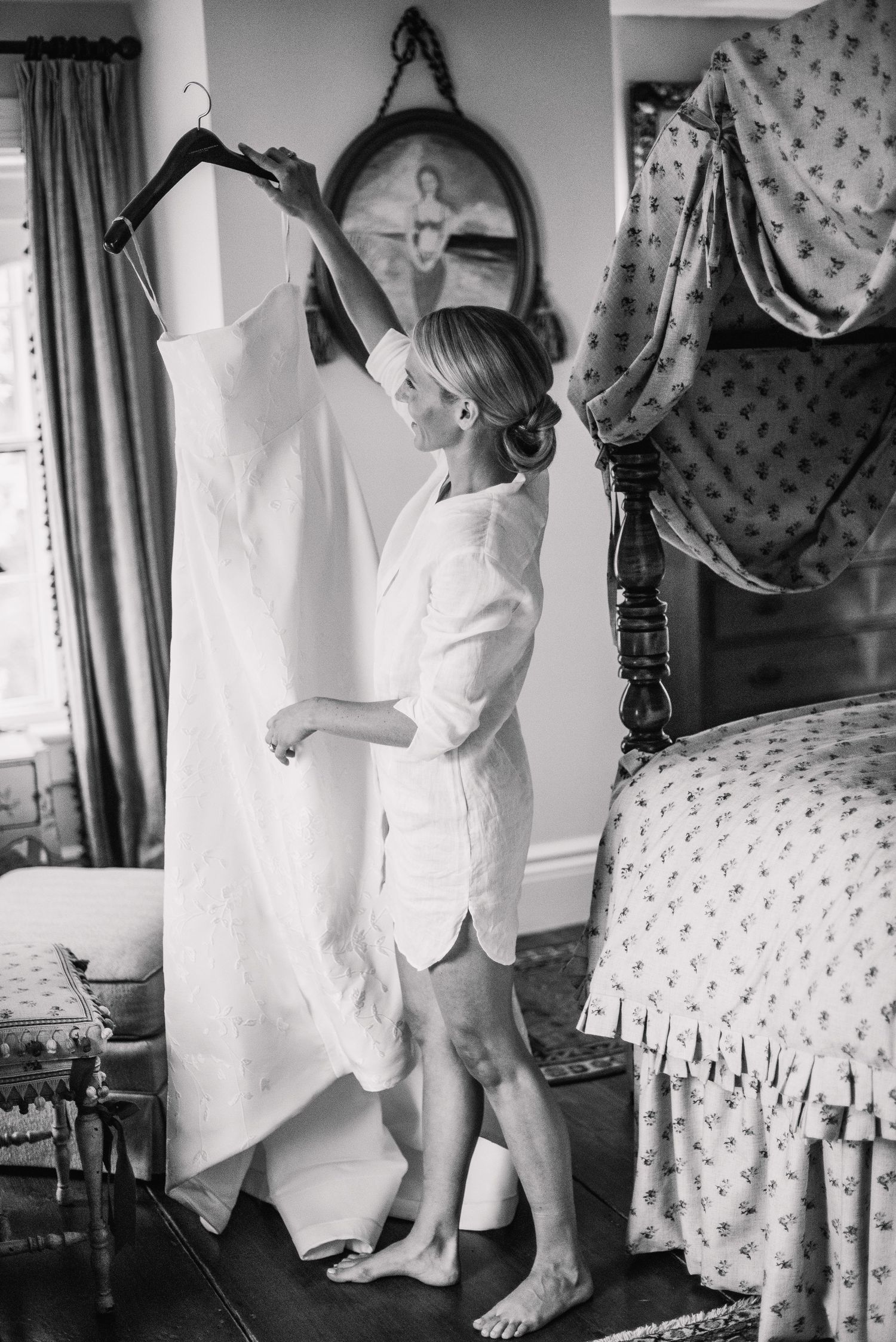Black and white photo of wedding preparations in a vintage-style bedroom with a white dress hanging.
