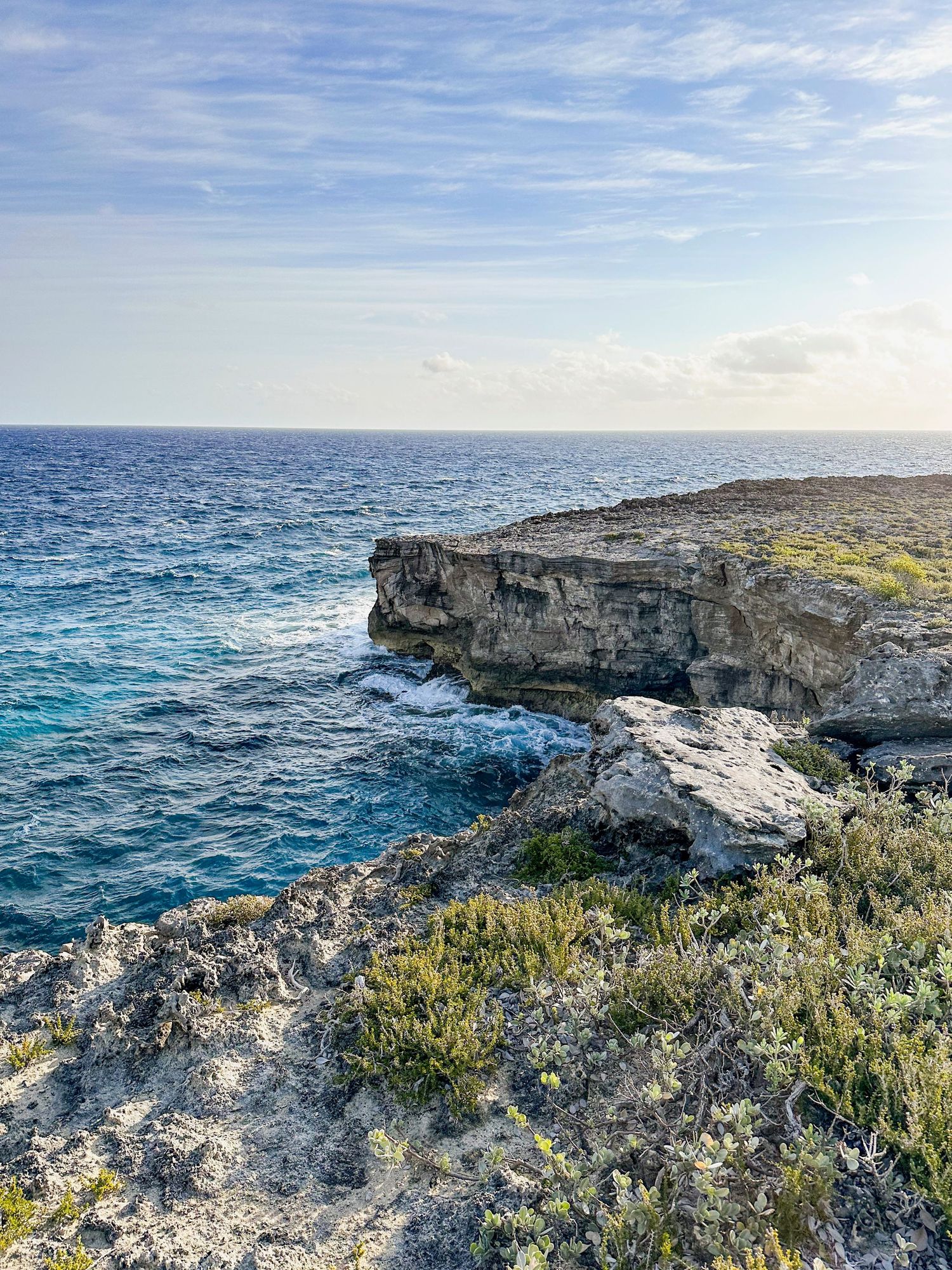 Rocky coastal cliffs overlooking turquoise Mediterranean waters under bright blue skies.