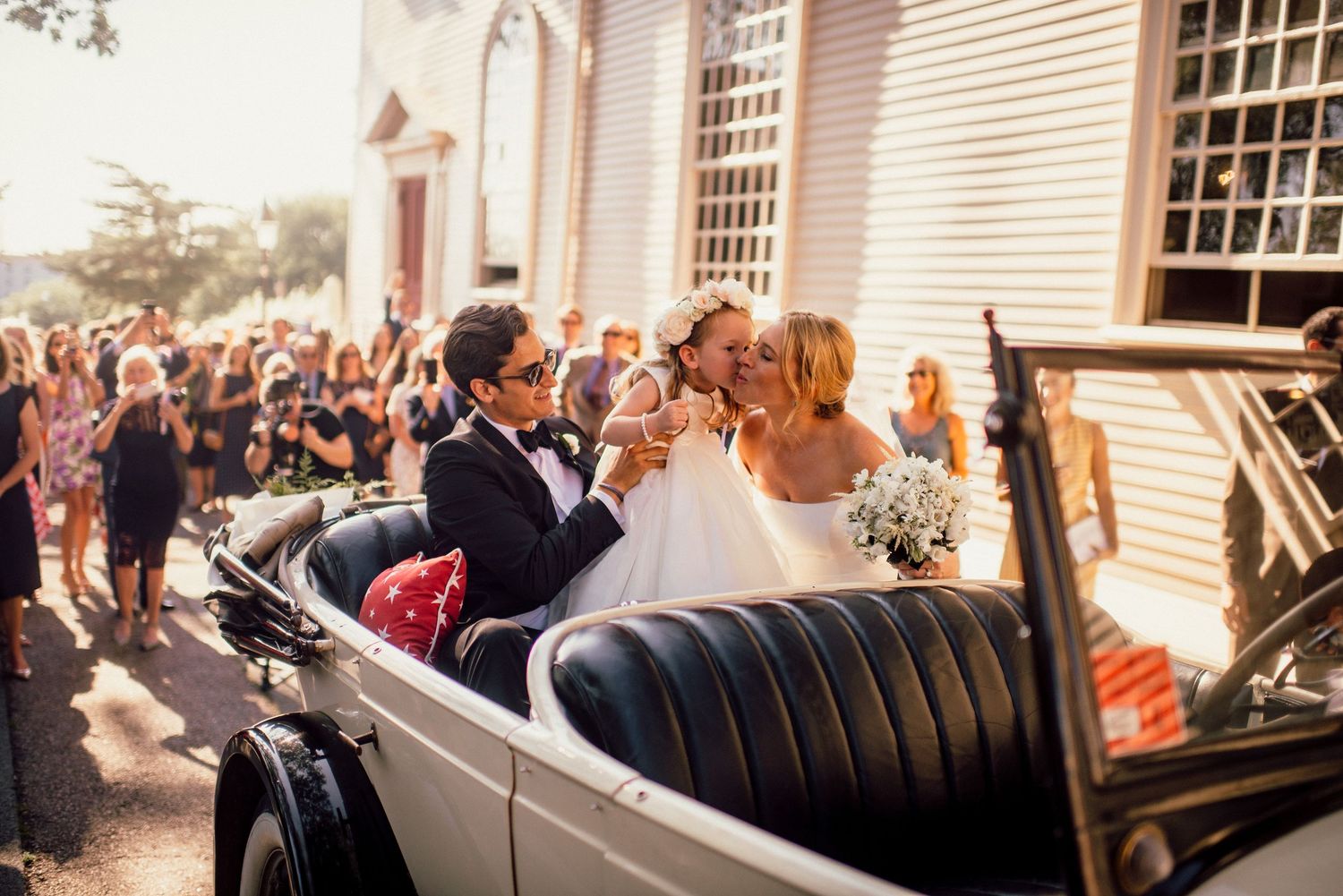 Wedding party celebrates with sparklers outside a white church building at dusk.