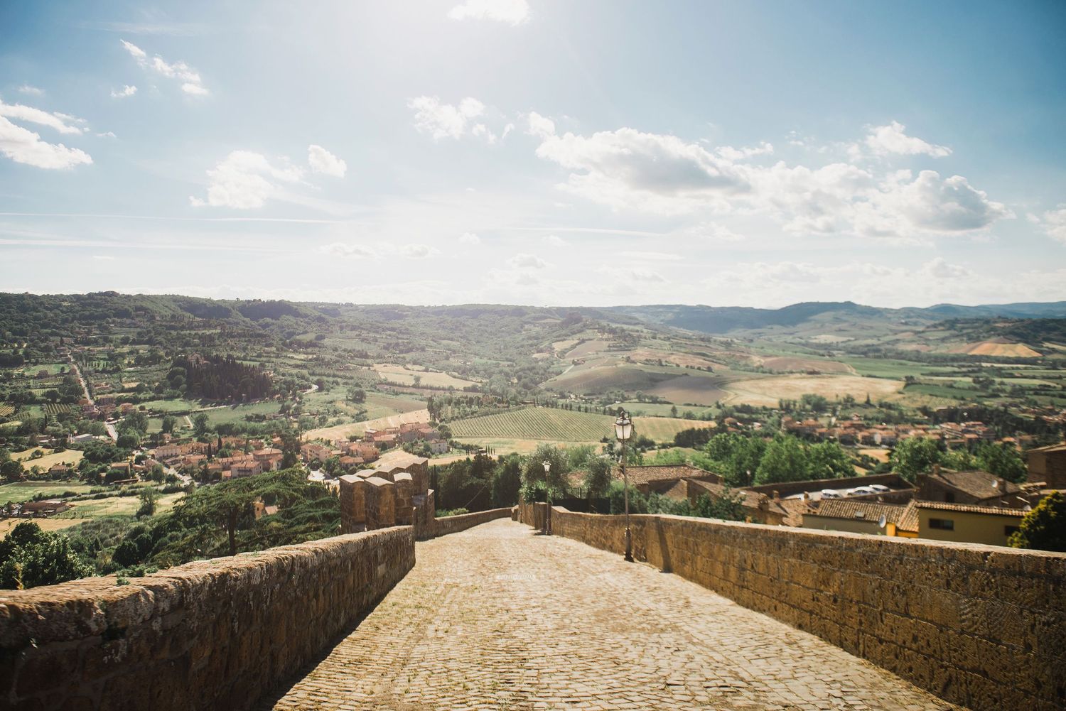 Wide panoramic view of Orvieto, IT from a stone fortress wall overlooking a coastal landscape and distant mountains.