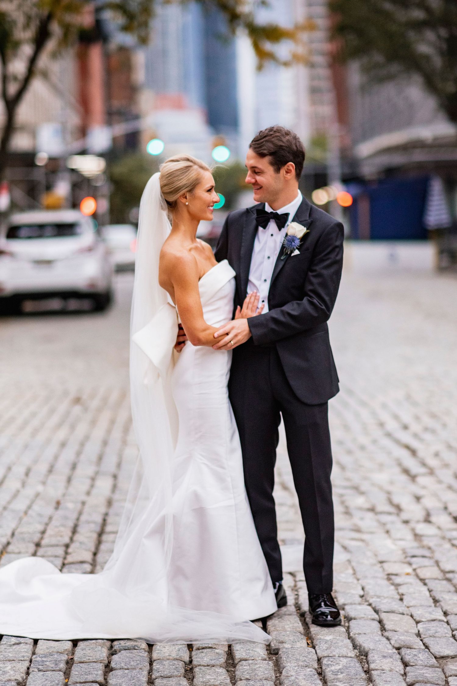 A wedding couple poses on cobblestone streets in formal attire.