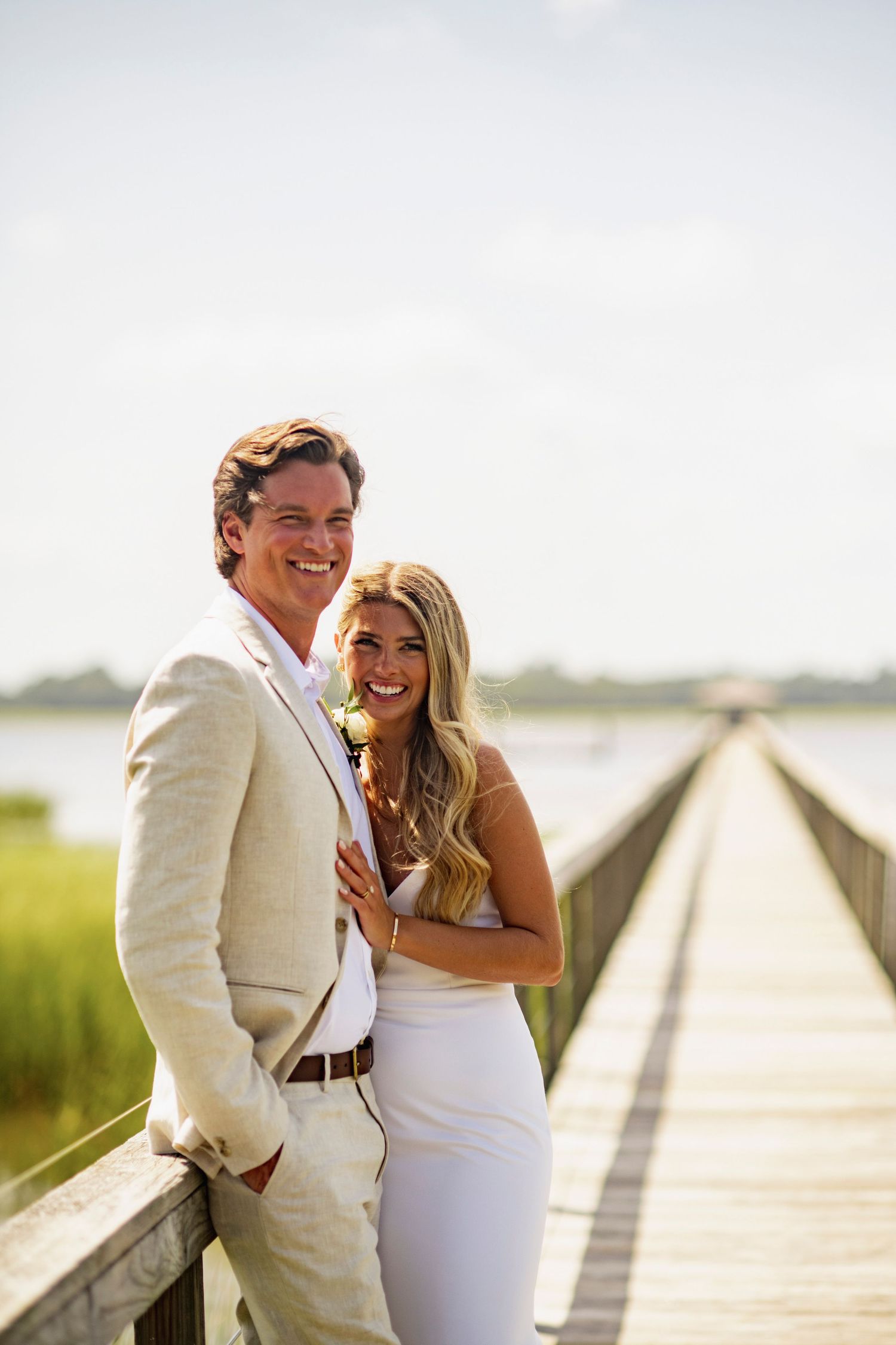 A couple shares joyful laughter together on a wooden boardwalk by the beach during a sunny day.