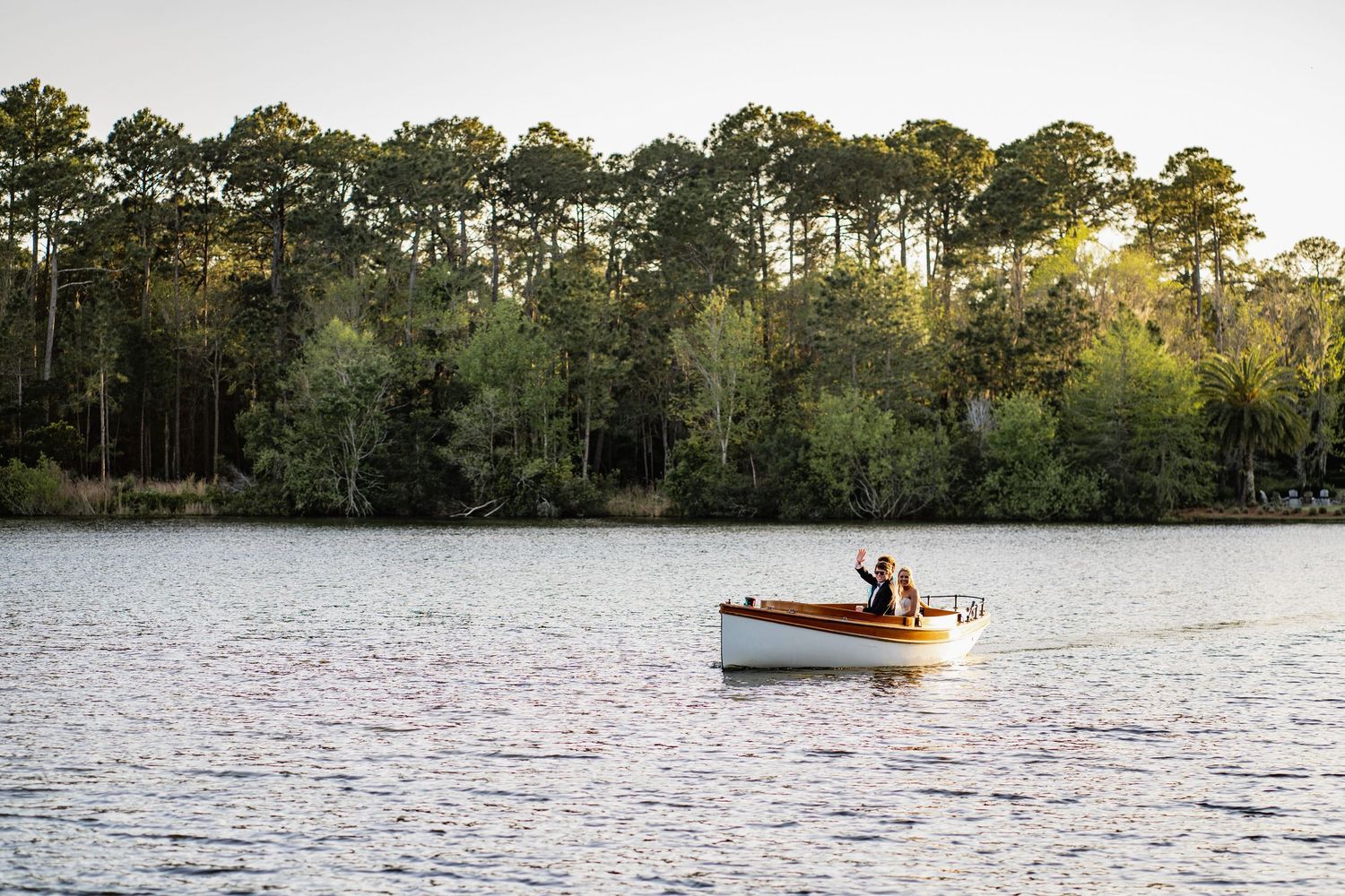 A boat glides across a serene lake surrounded by lush green trees on a sunny afternoon.