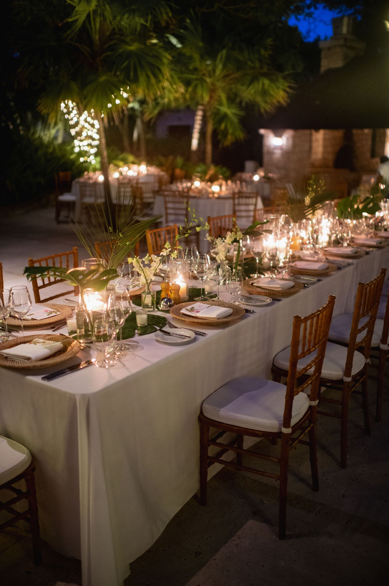Elegant candlelit wedding reception tables set with white linens and wooden chairs.