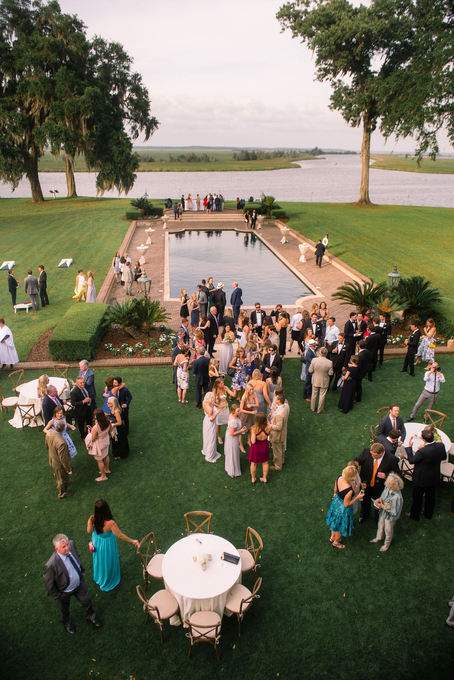 Wedding guests gather on a scenic waterfront lawn during an outdoor reception celebration near a lake.
