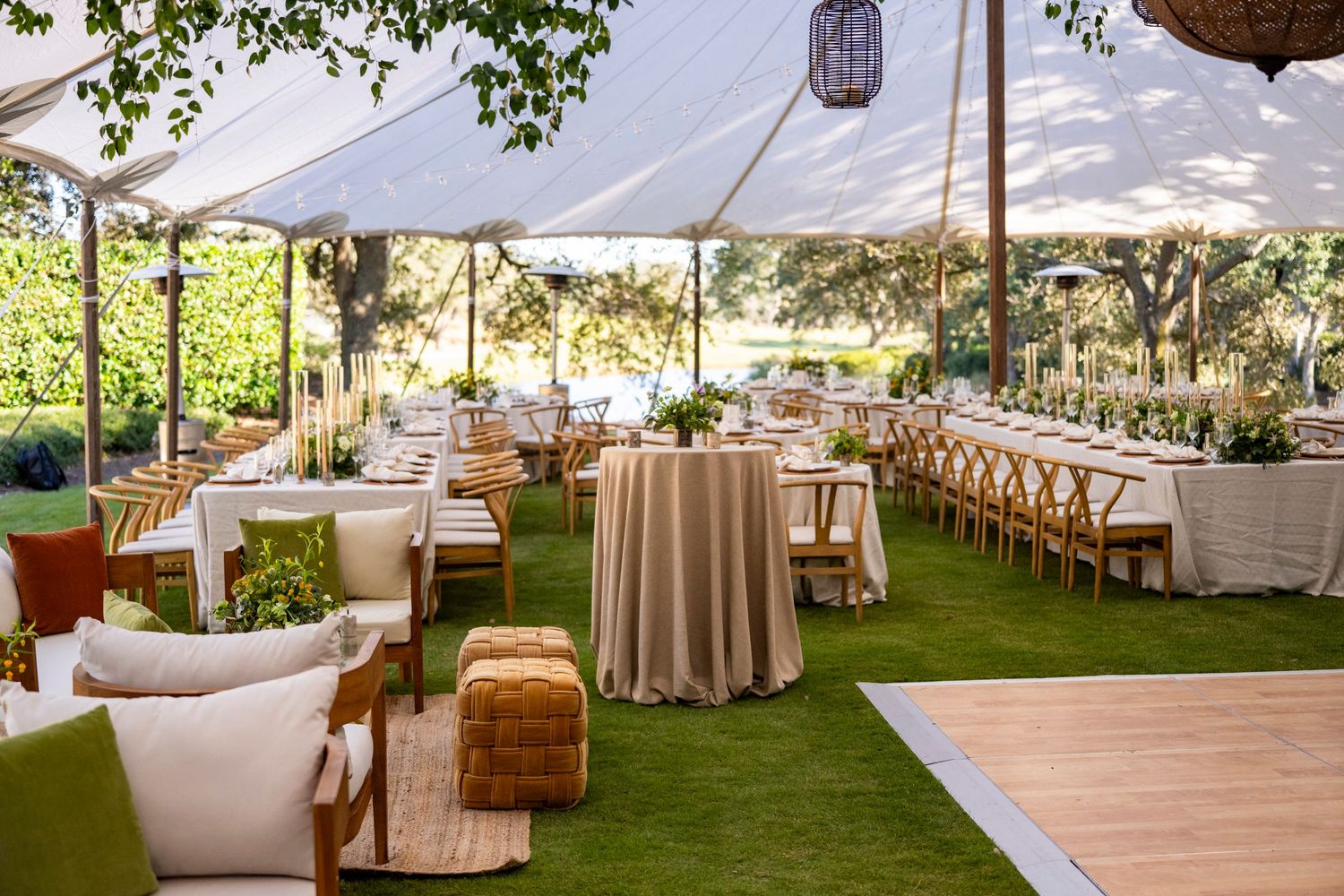 Elegant outdoor wedding reception setup with white tents, round tables, and natural decor in a garden setting.