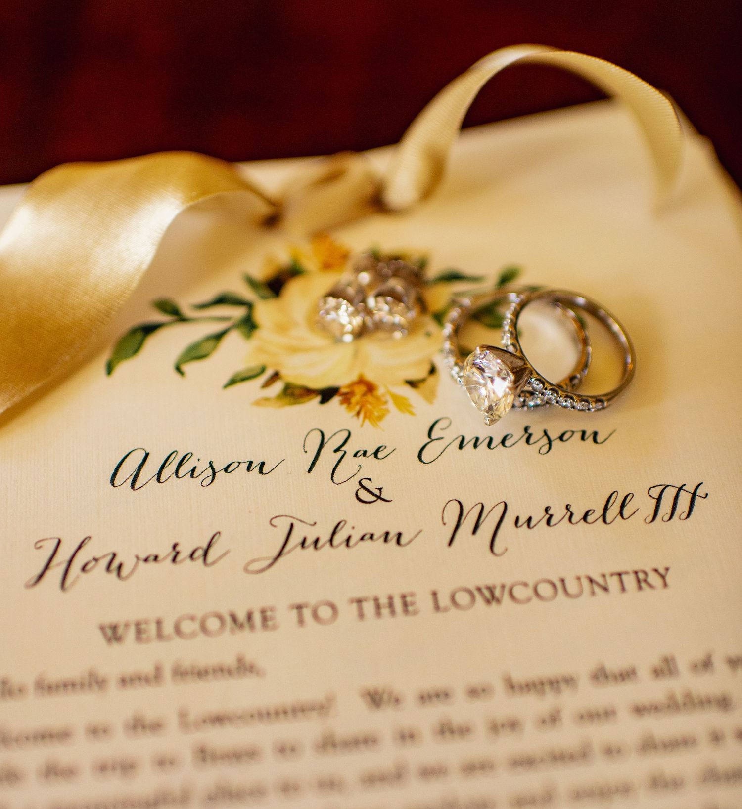 Wedding rings and invitation card with elegant calligraphy welcoming guests to the Lowcountry rest on cream fabric.