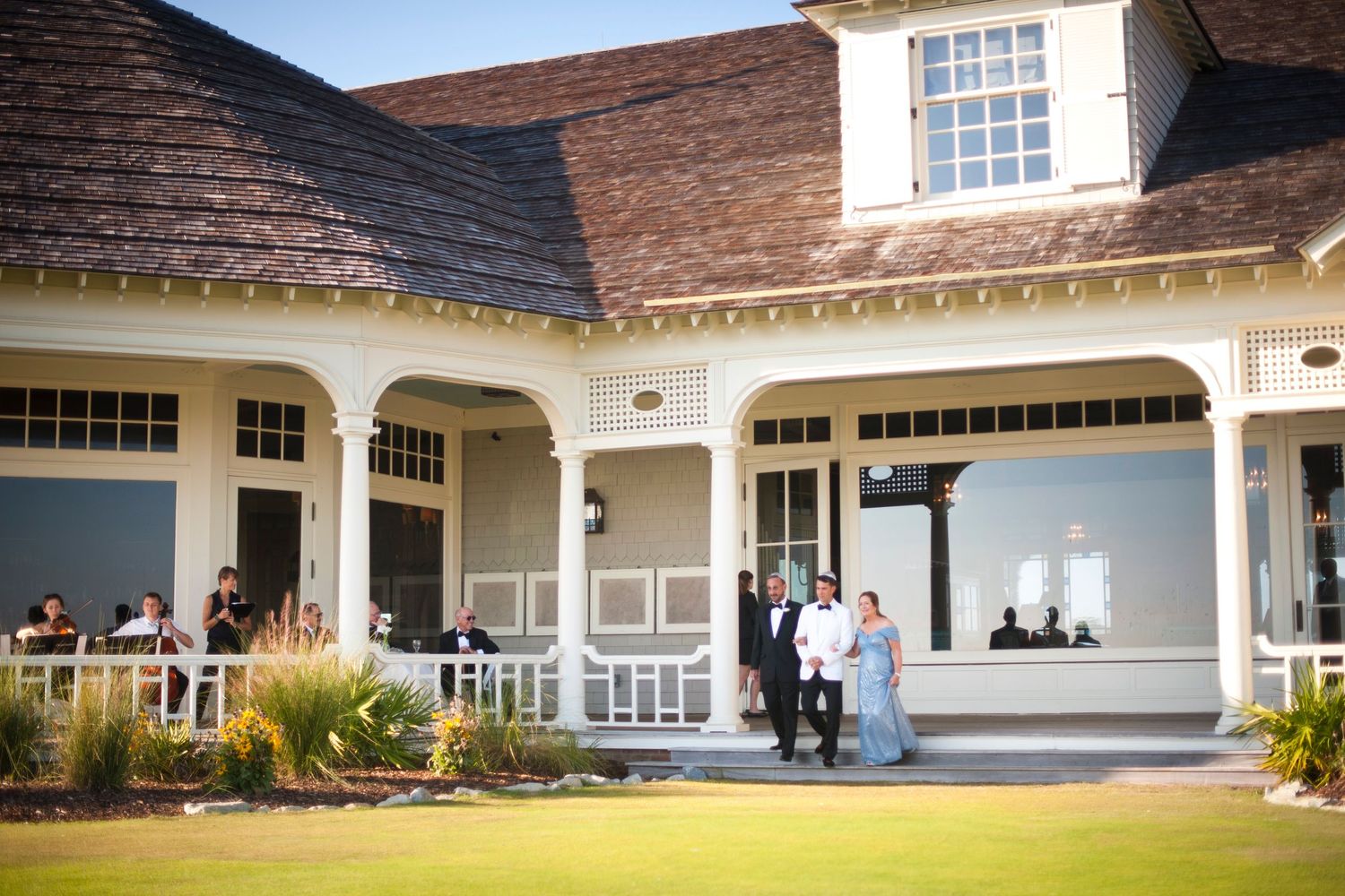 A panoramic view of a white colonial-style country club building with covered porches and manicured landscaping.
