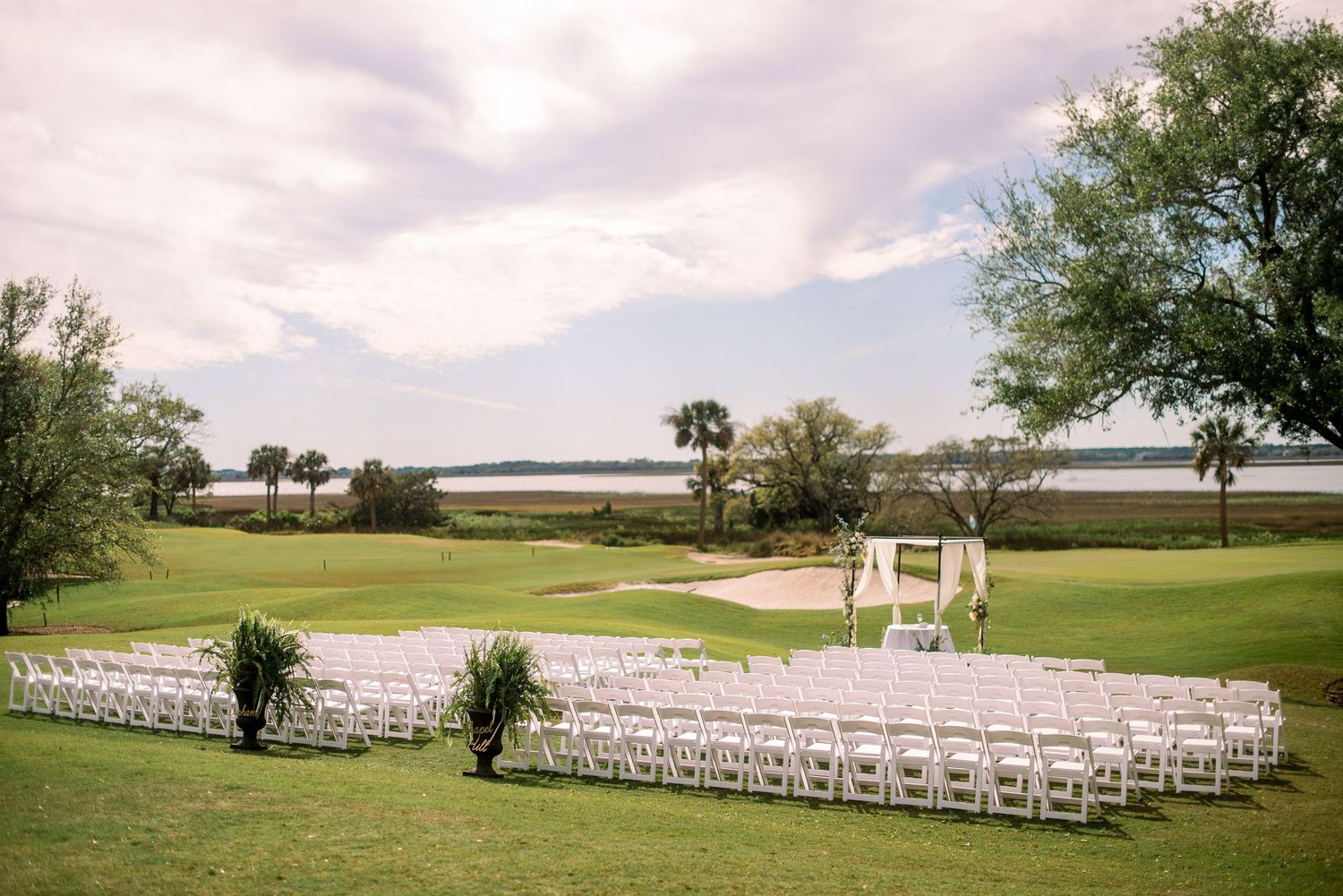 White chairs arranged in rows for an outdoor wedding ceremony on a lush green lawn with trees in the background.