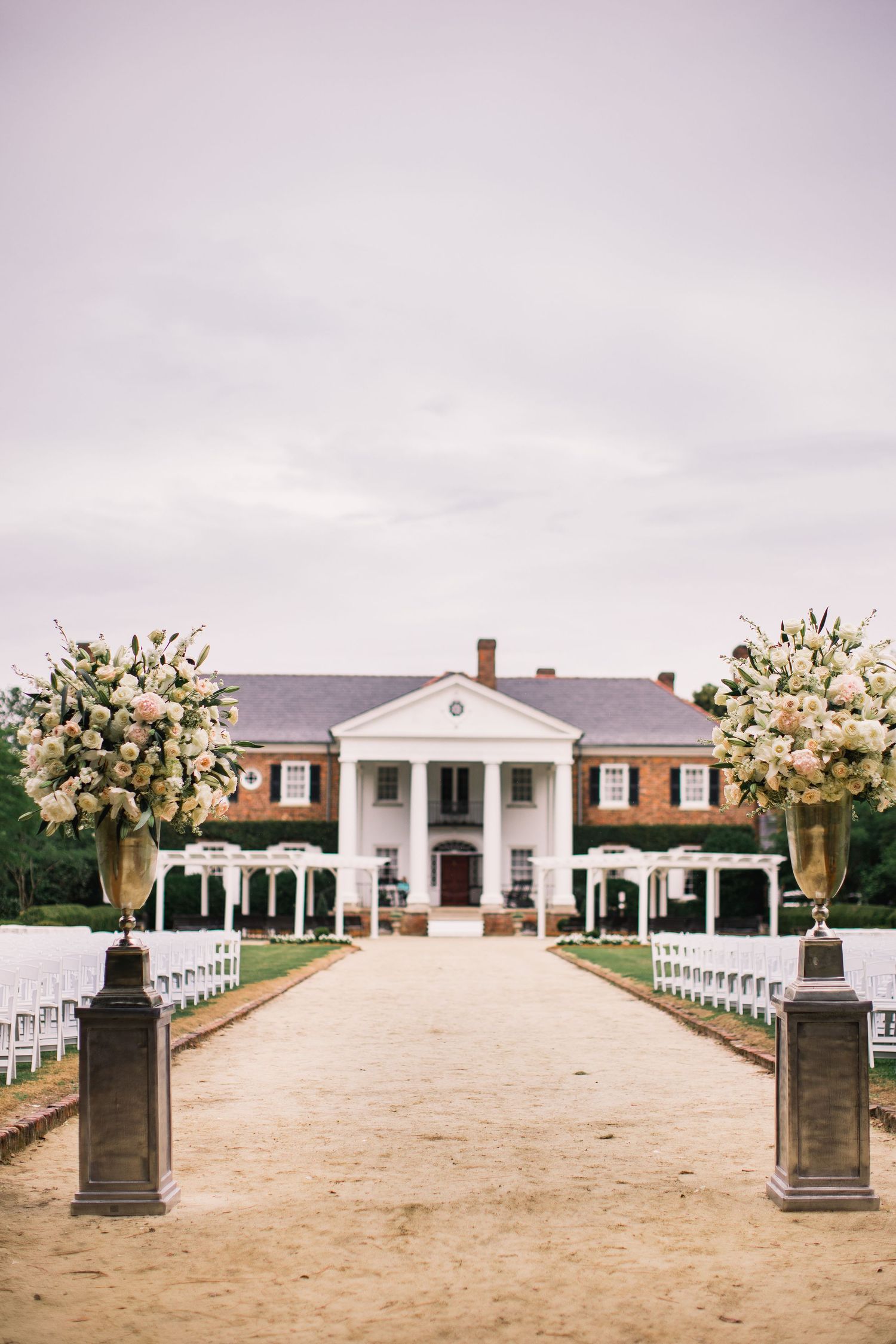 Panoramic view of an elegant white Southern mansion with brick facade and pillars set up for an outdoor wedding ceremony.