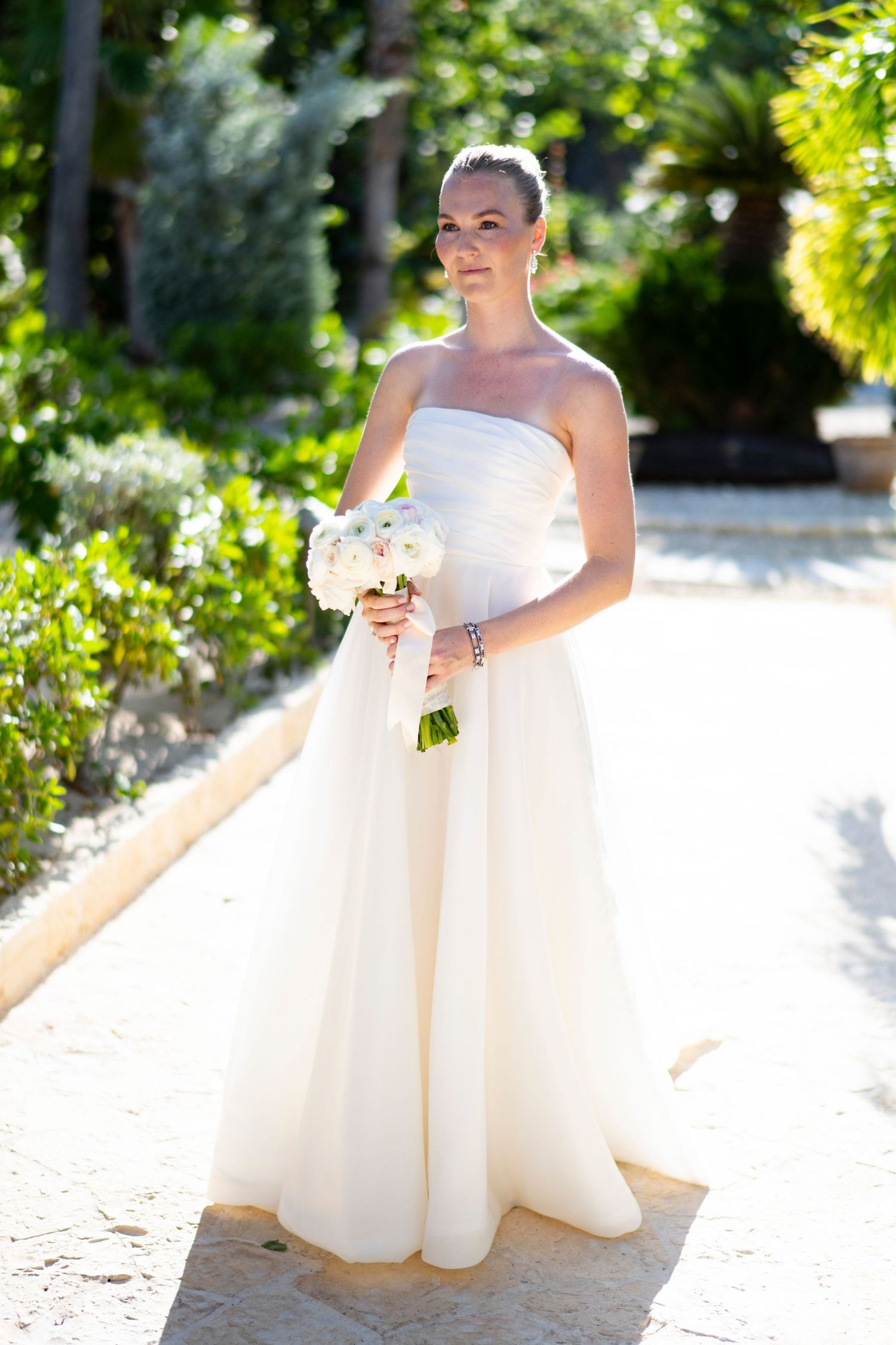 Elegant white wedding gown with flowing tulle skirt photographed in a garden setting.