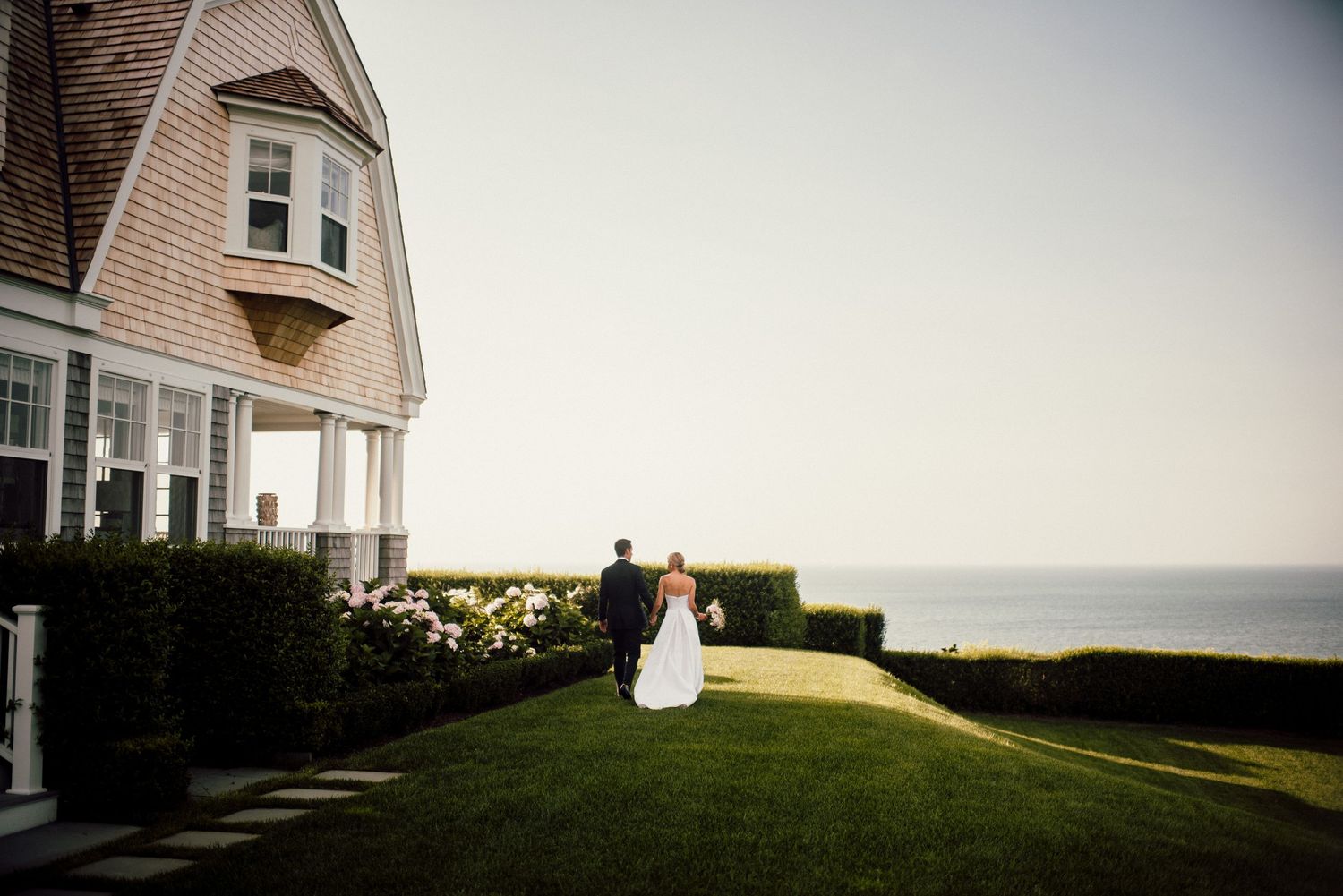 Distant view of couple sitting on grass overlooking the ocean at sunset.