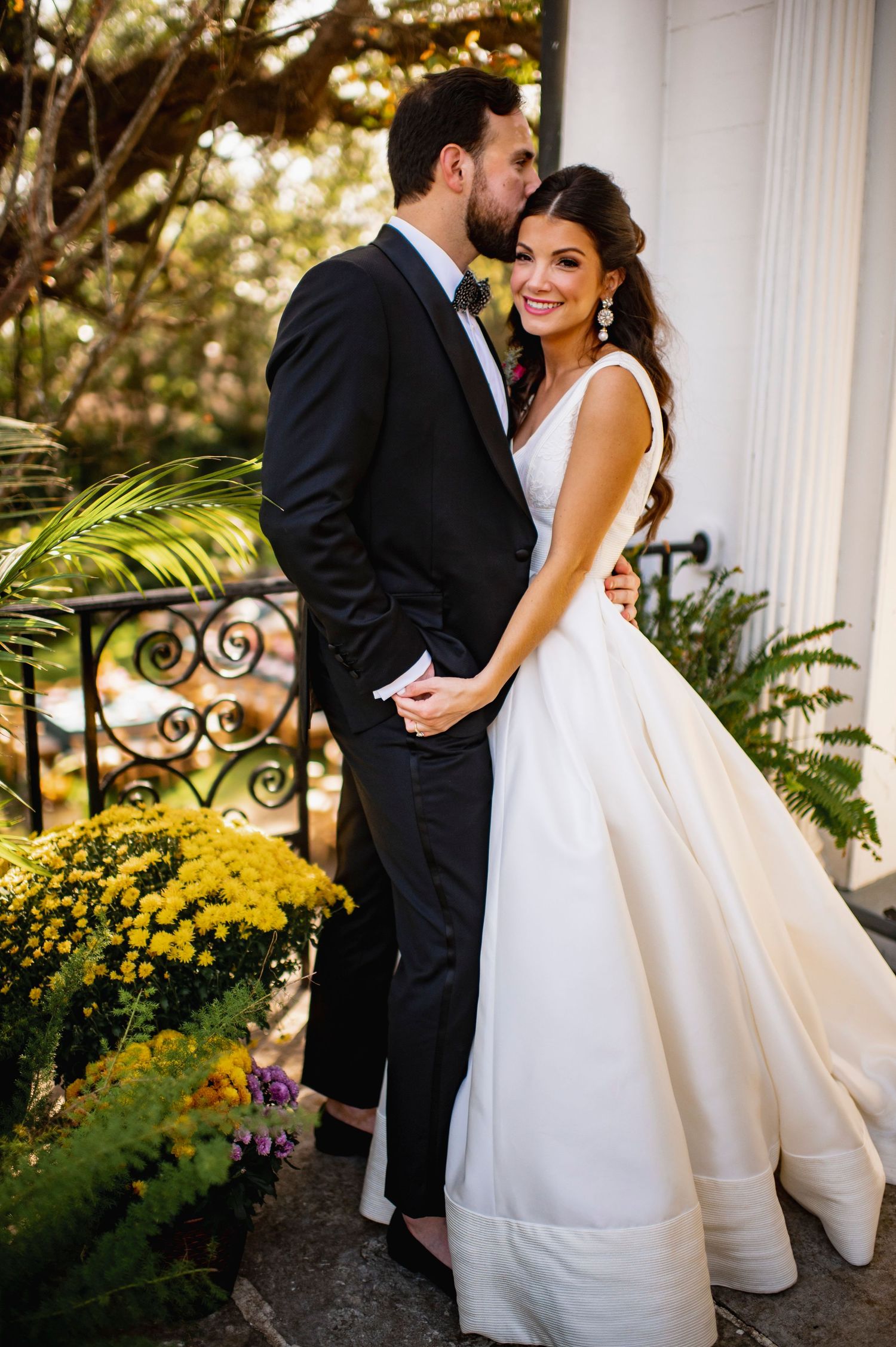 Elegant wedding couple embracing by white columns in garden setting.