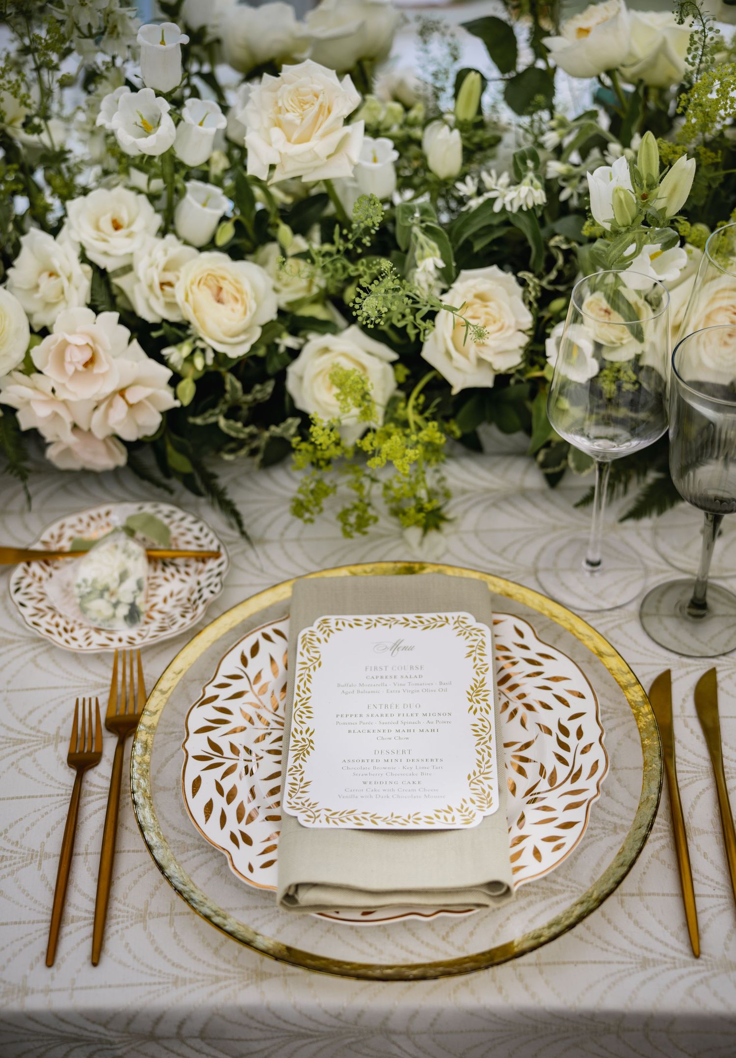 Elegant table setting with gold chargers, white floral centerpieces and laser-cut menu cards.