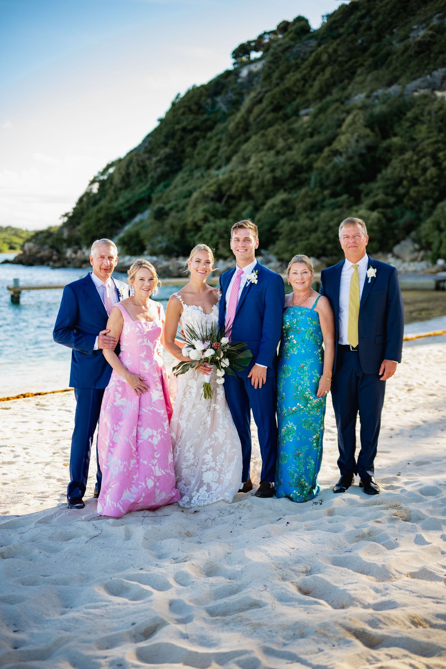 Wedding party poses on a scenic beach at sunset with mountains in the background.