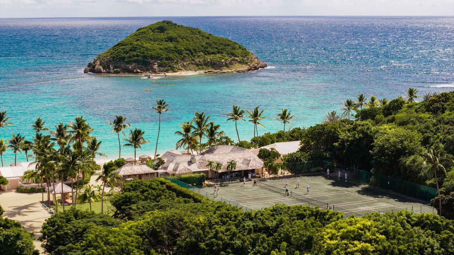 Aerial view of a tropical beach with palm trees and turquoise waters surrounding a small island.