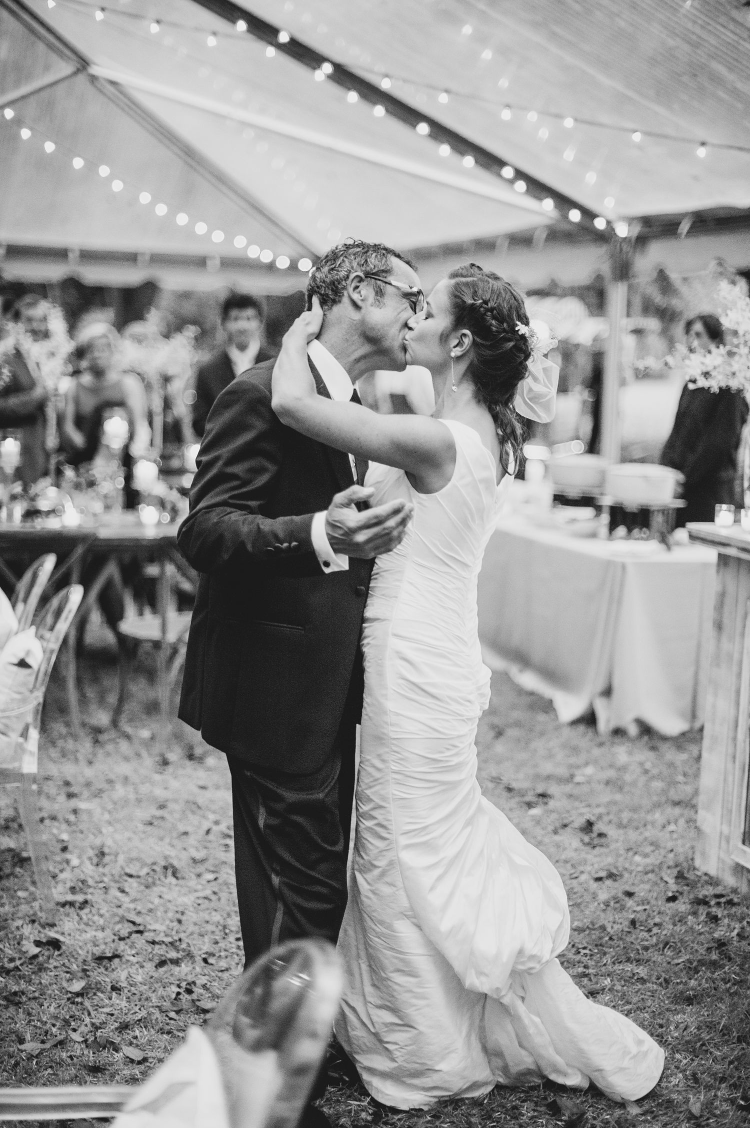 A couple shares a romantic dip dance moment under a white tent at their outdoor wedding reception.