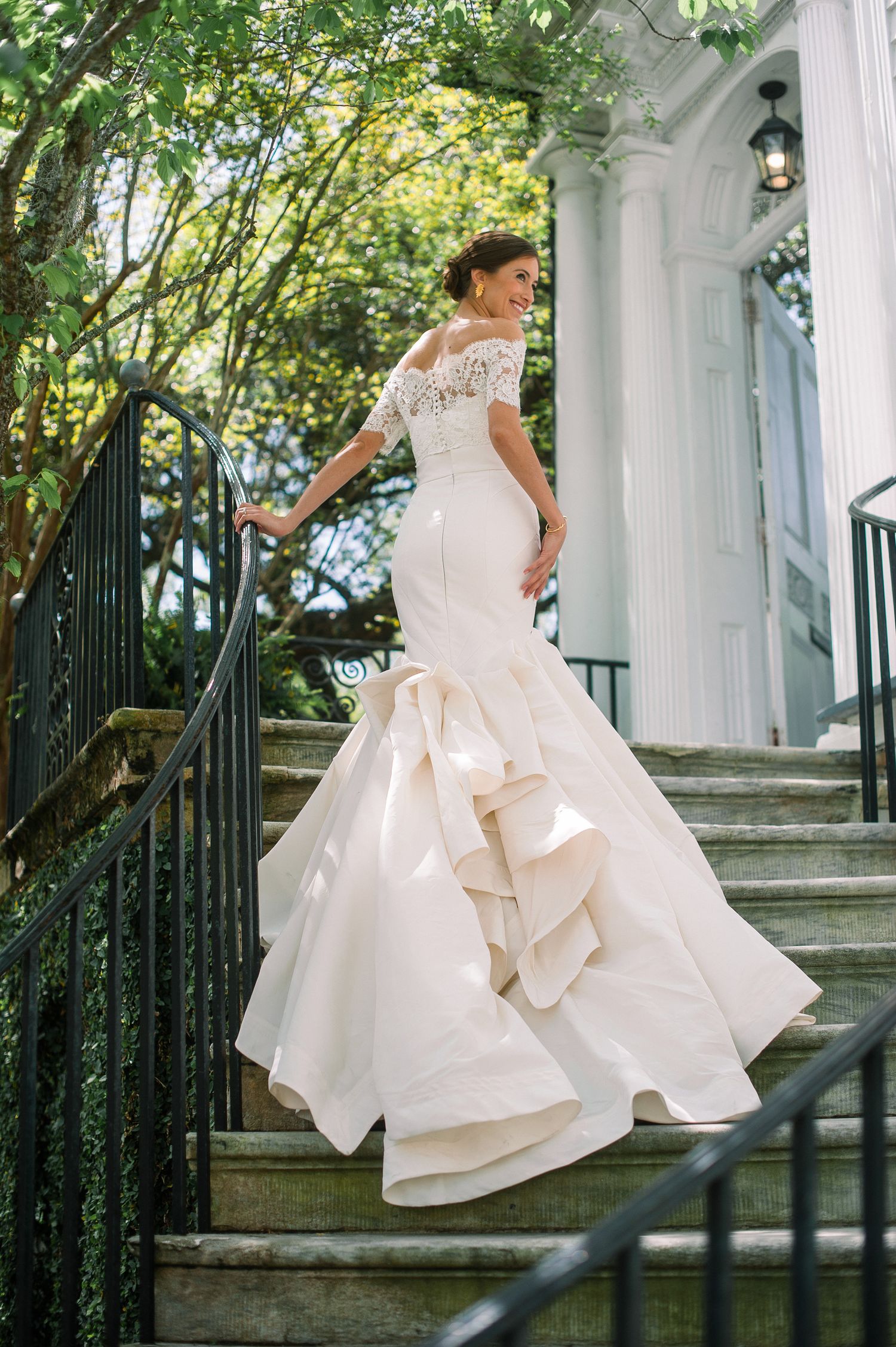 A stunning mermaid-style wedding dress with lace bodice and ruffled skirt cascades down grand outdoor stone steps.