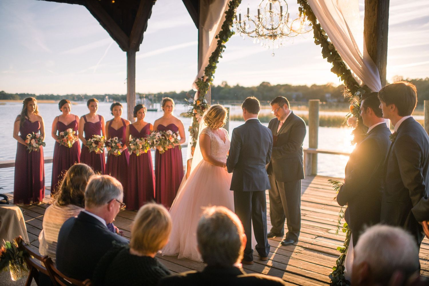 Wedding ceremony setup on a waterfront dock at golden hour with guests seated facing the water.