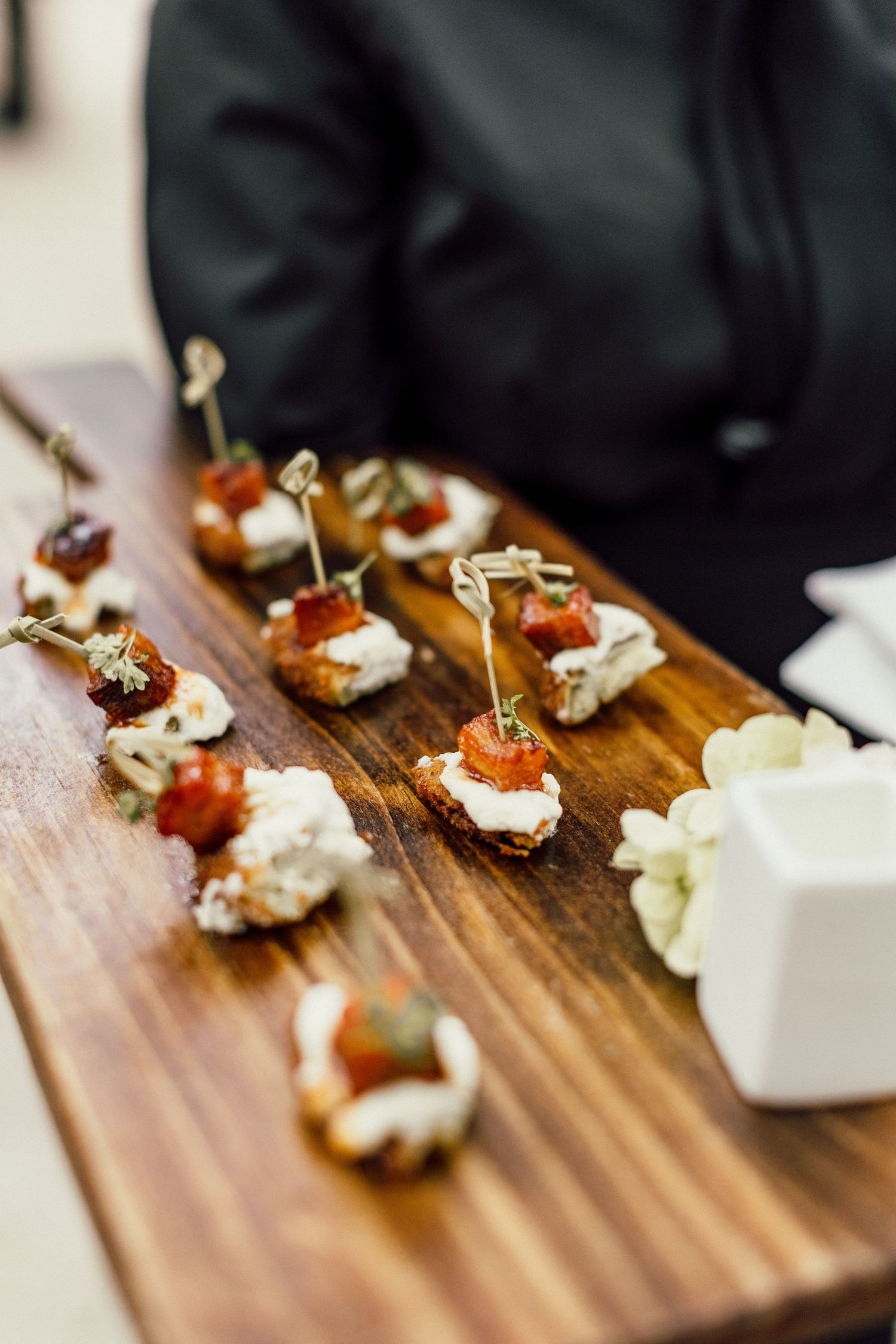Small gourmet appetizers with white cream and garnishes served on a rustic wooden serving board.