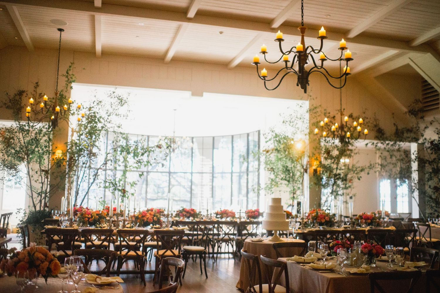 An elegant wedding reception venue with rustic chandeliers and tables decorated with autumn floral centerpieces.