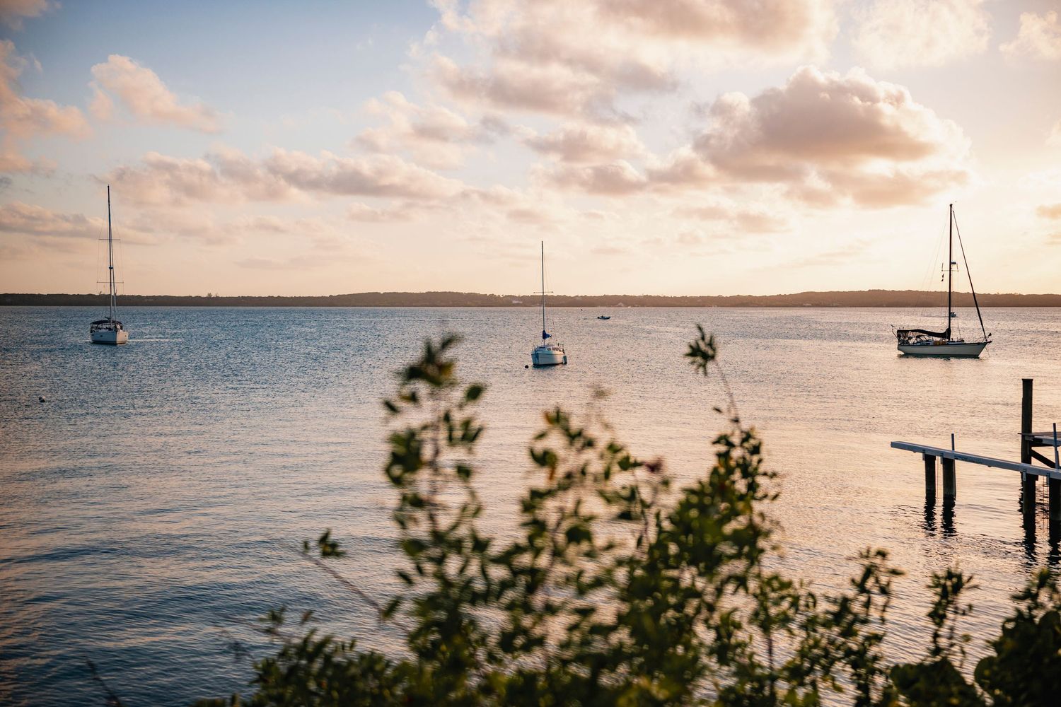 Sailboats anchored in calm waters at sunset with golden clouds reflecting on the tranquil ocean surface.