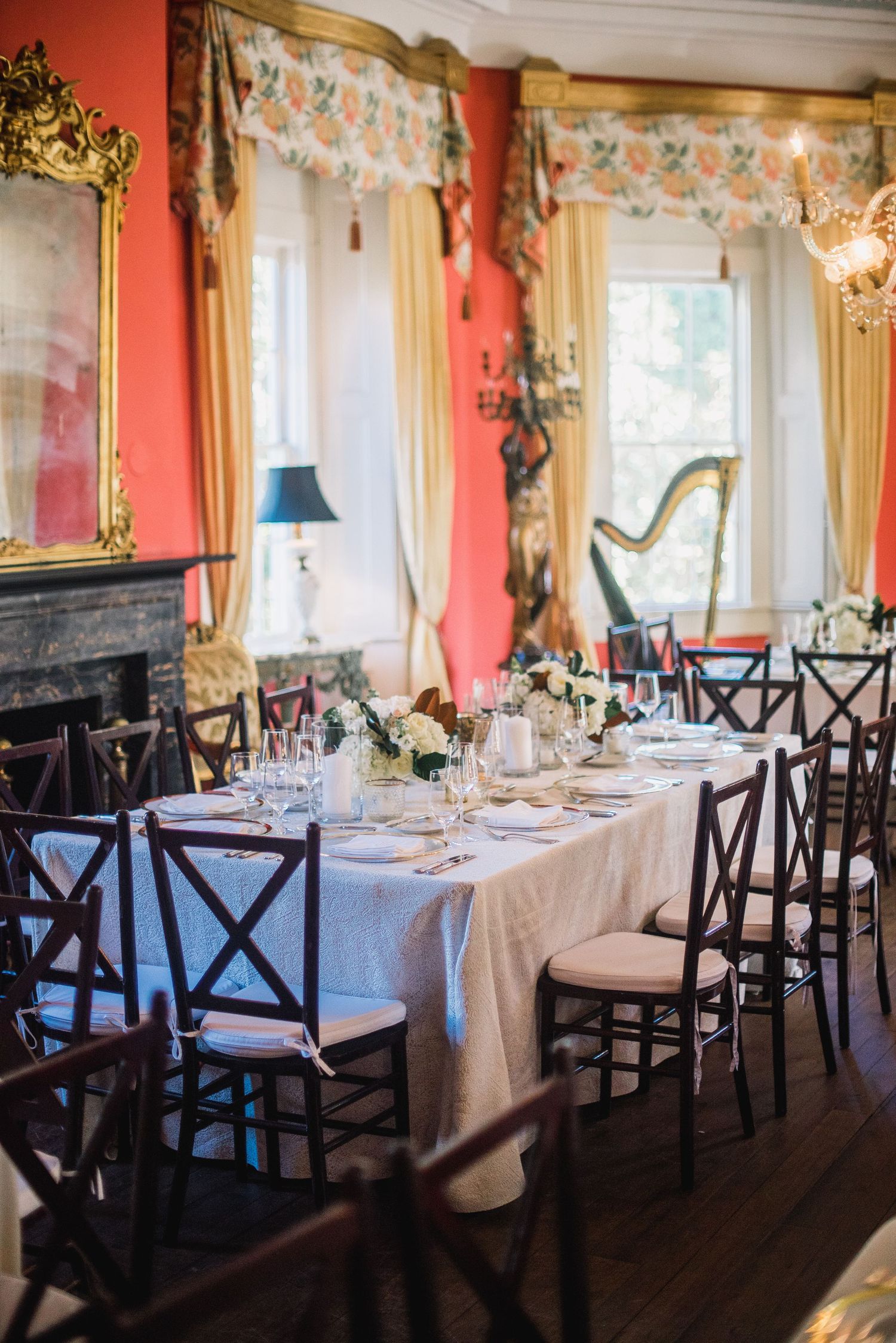 Formal dining room with red walls, white tablecloths, and black cross-back chairs set for an upscale event.