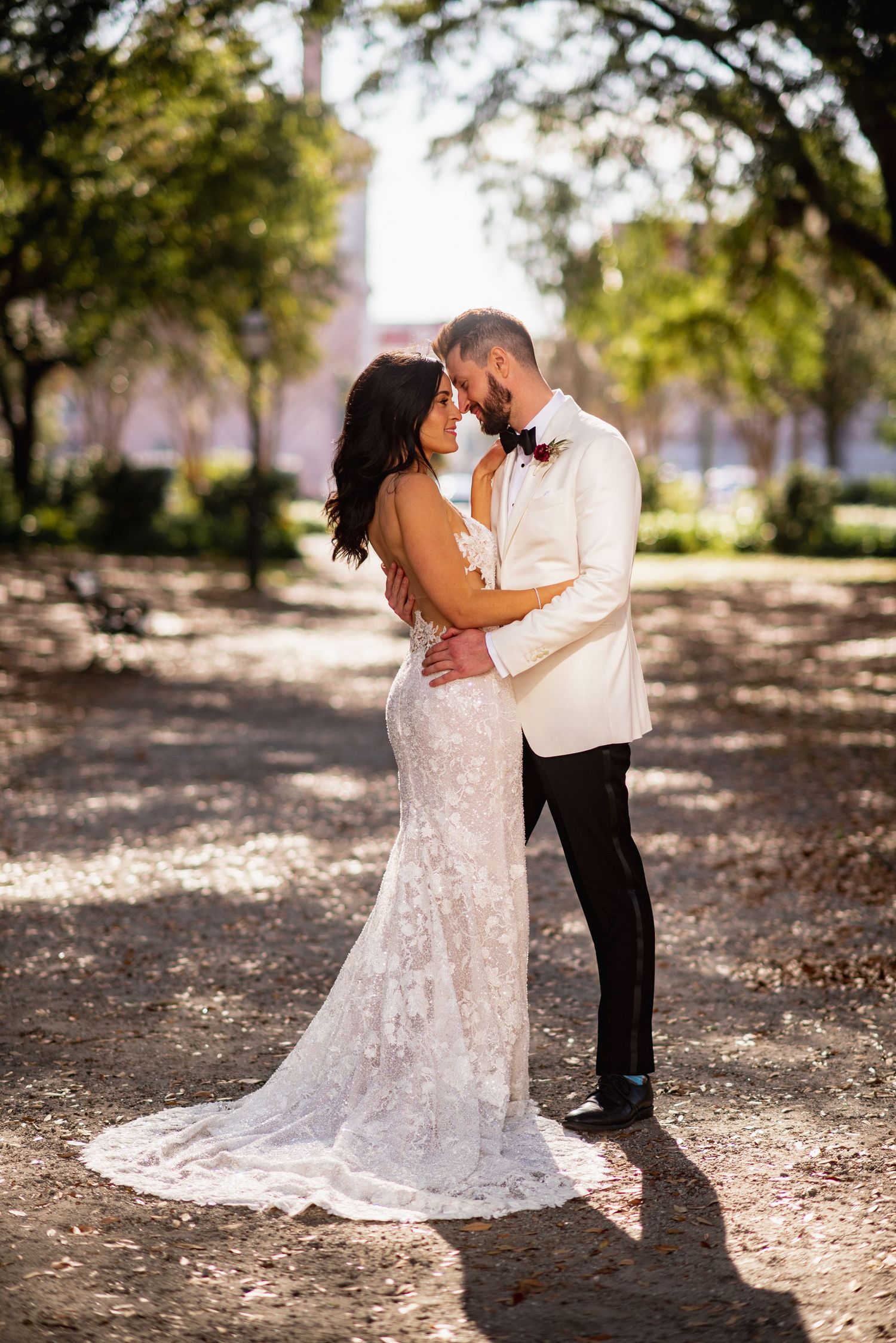 Romantic outdoor wedding portraits under sunlit trees with a flowing white lace gown.