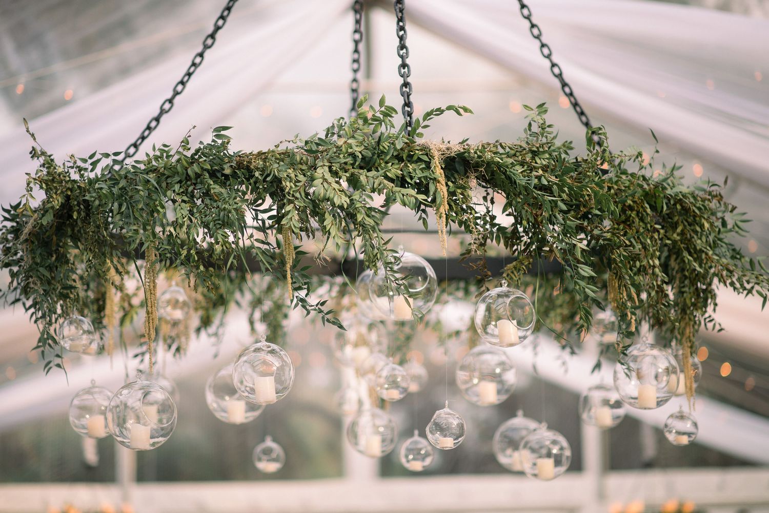 Delicate glass baubles and greenery hang from a white draped ceiling creating an elegant wedding reception atmosphere.