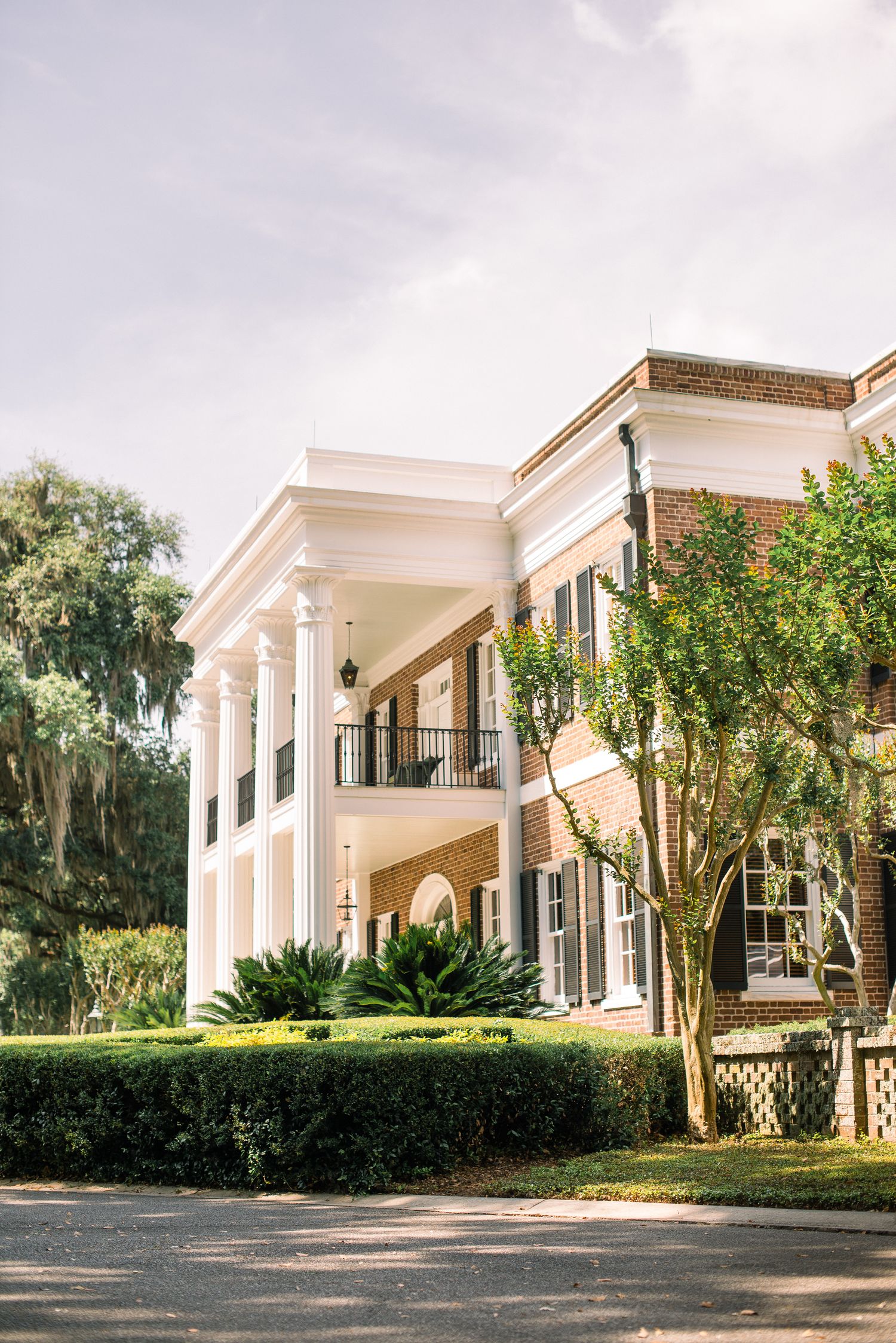 Elegant Southern mansion with white columns and brick exterior showcases classic antebellum architecture in a lush garden setting.