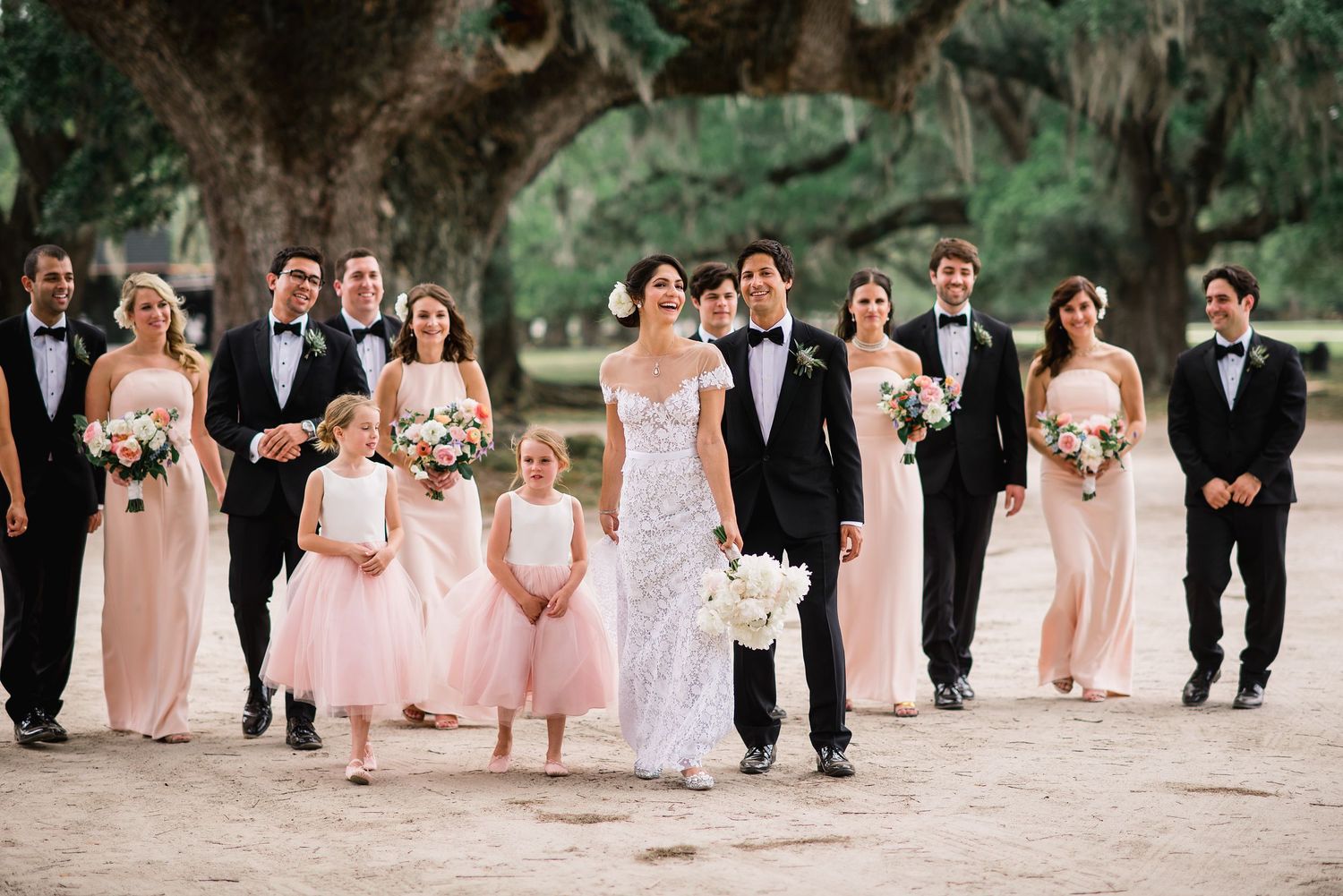 Wedding party in pink dresses and black tuxedos walking in a line outdoors.