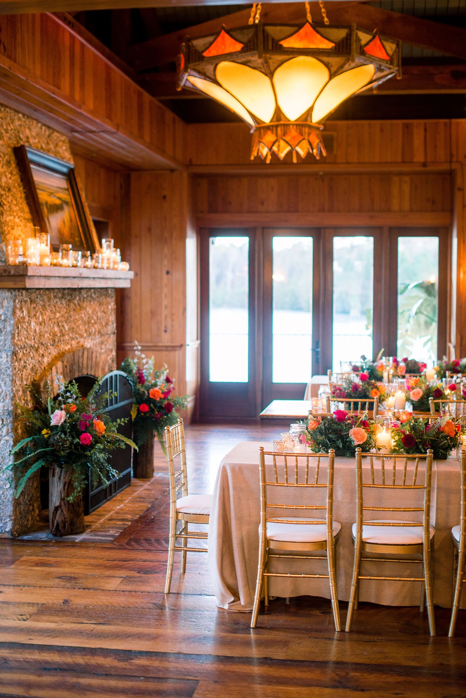 Rustic wooden reception hall with elegant table settings and floral centerpieces illuminated by warm pendant lighting.