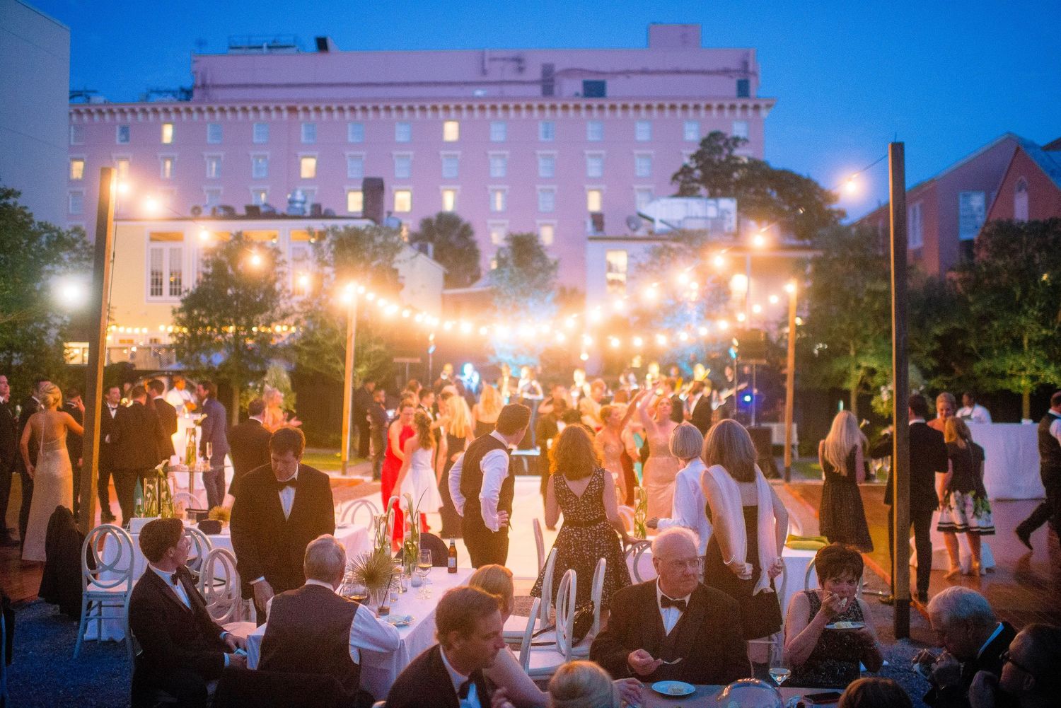 A series of outdoor wedding reception photos showing guests dancing and celebrating under string lights at dusk.