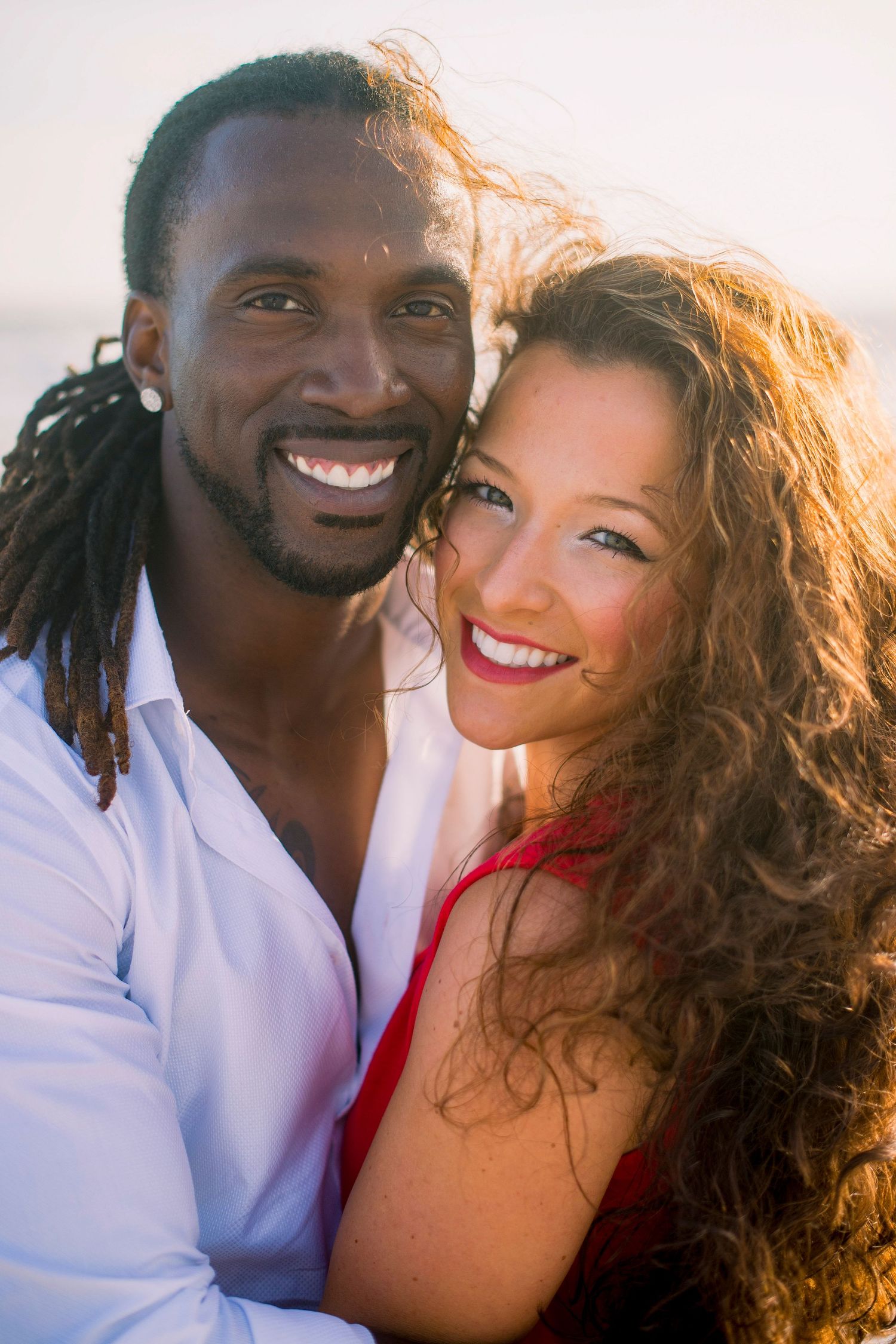 A romantic sunset photoshoot featuring a couple embracing and laughing together on a beach.