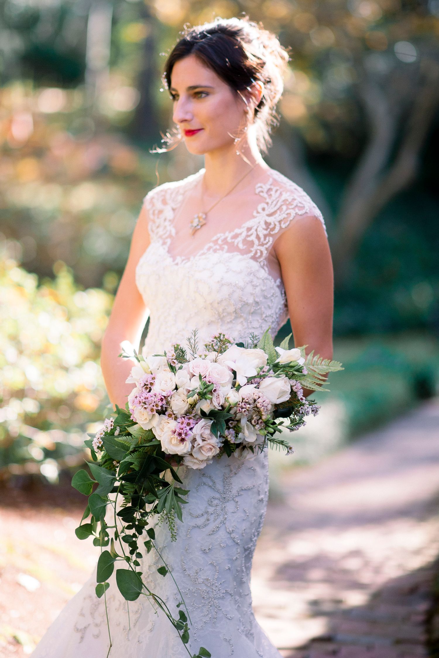 Bride in lace wedding dress holding a romantic bouquet of pink and white flowers with greenery.