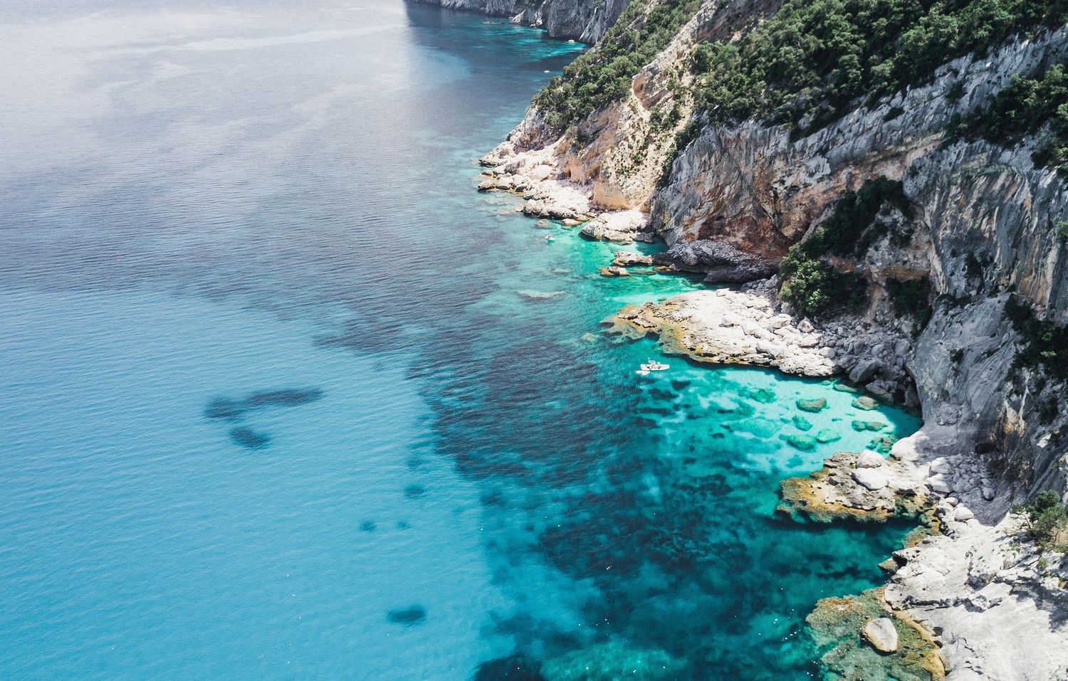 Dramatic rocky coastline with steep cliffs dropping into vibrant turquoise Mediterranean waters.