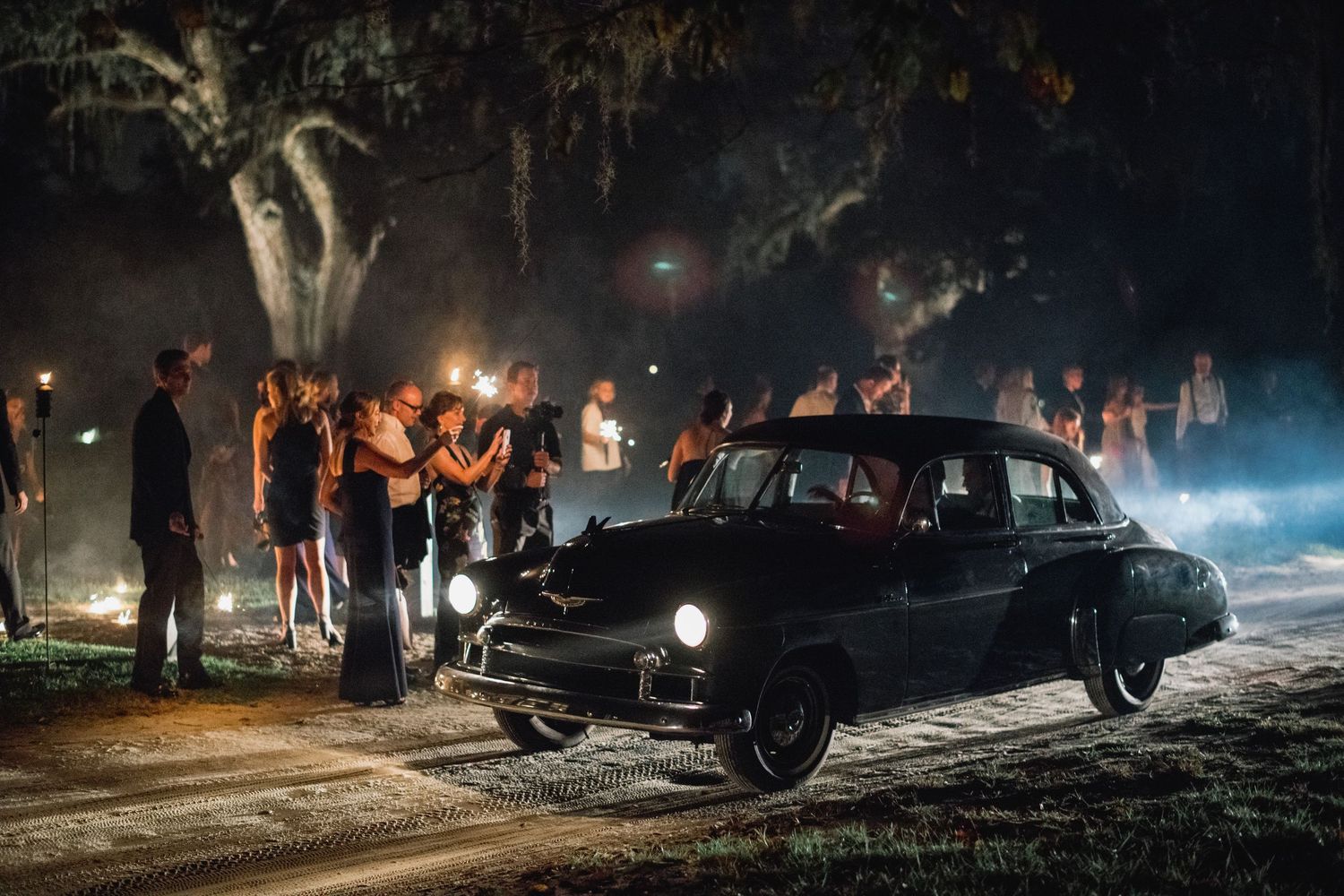 A dramatic nighttime scene shows several dark vehicles illuminated by atmospheric fog and street lights.