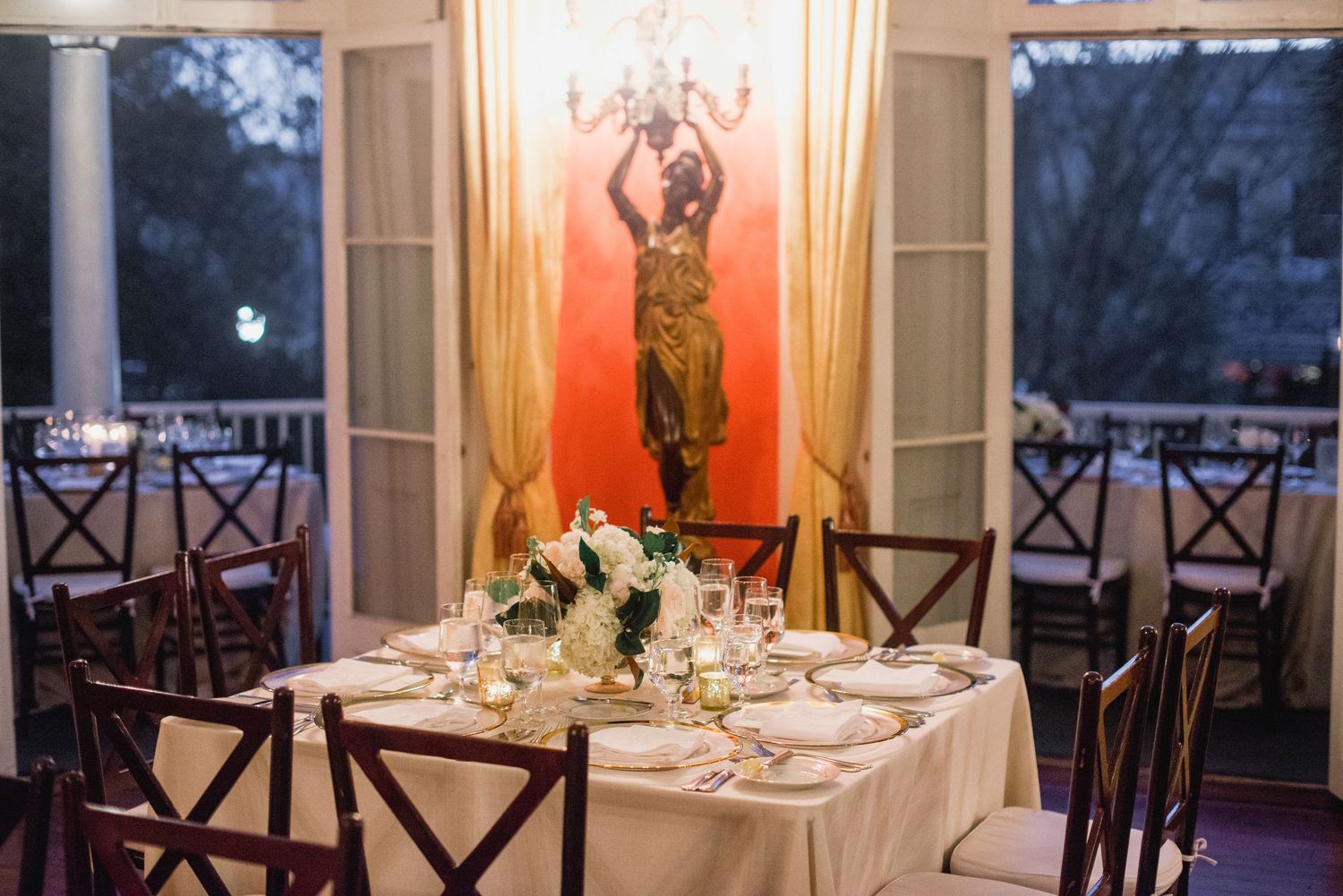 Elegant wedding reception venue with white tablecloths, dark wood chairs, and warm lighting creating a romantic atmosphere.