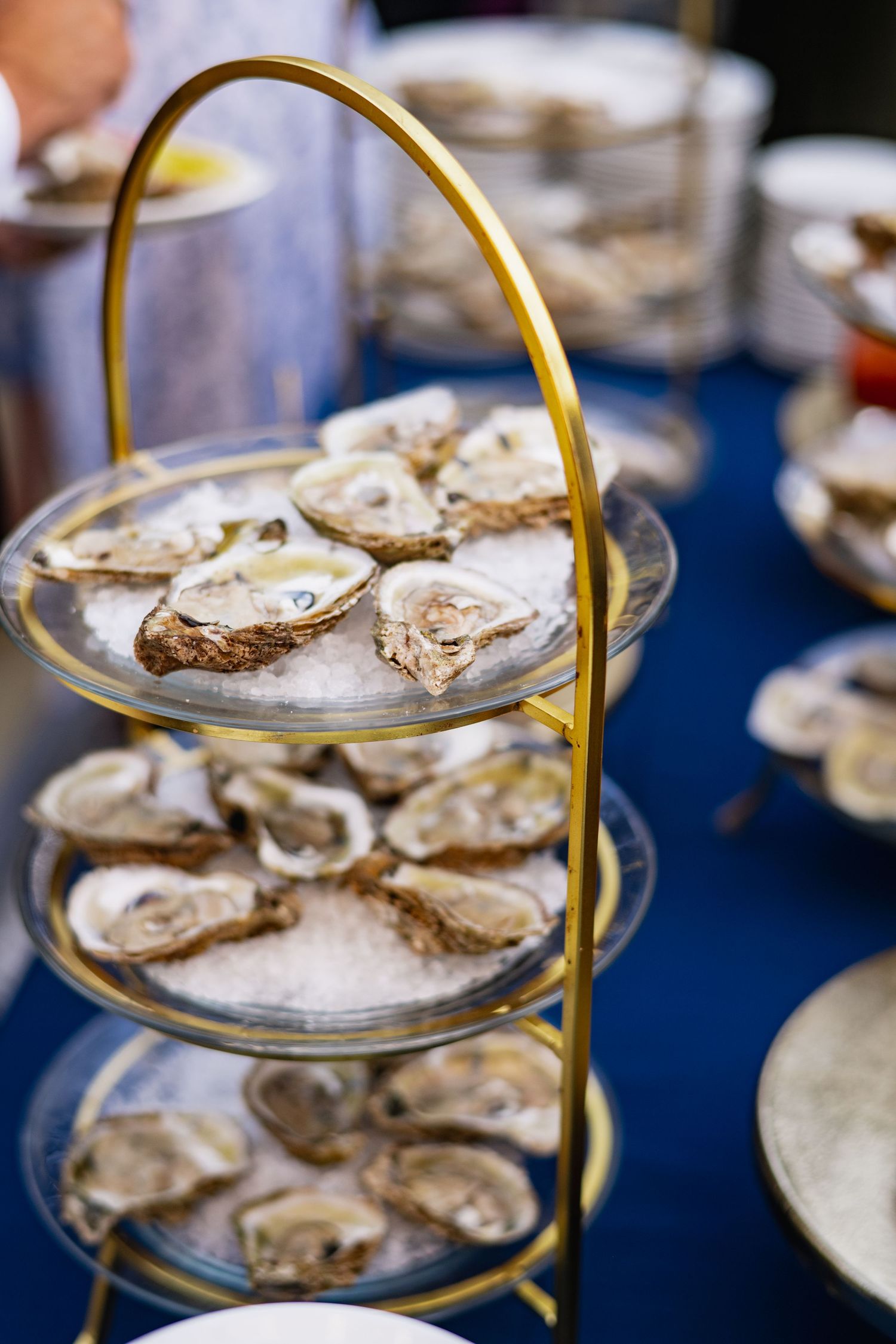 Fresh oysters on ice displayed on elegant gold-rimmed tiered serving platters at an upscale event.