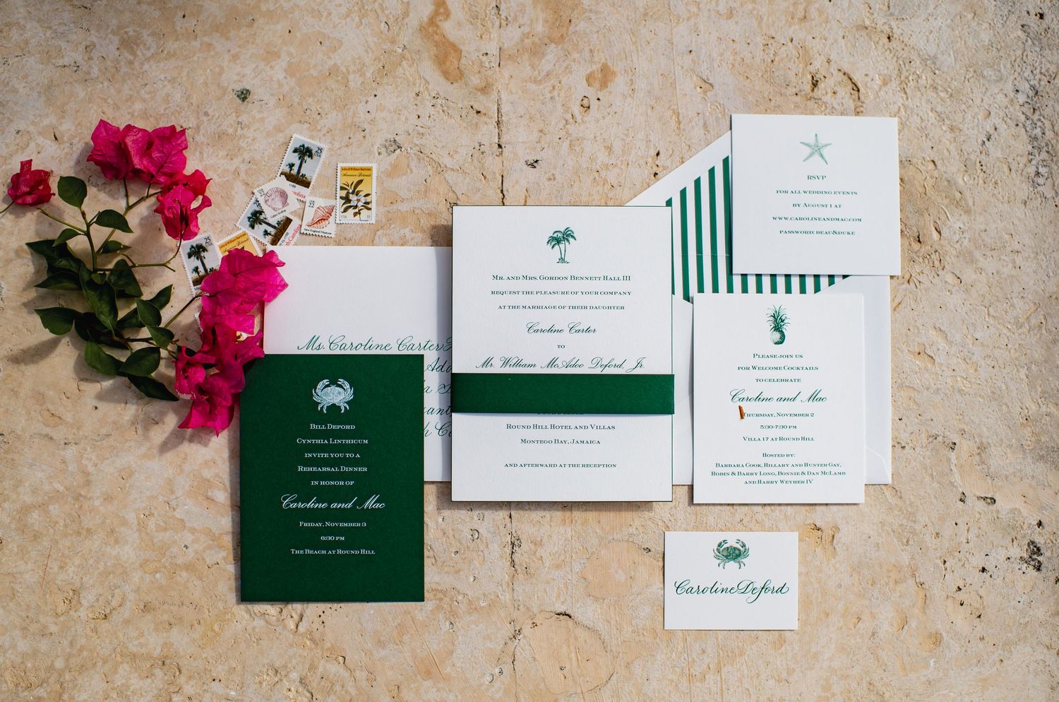 Wedding invitation suite with emerald green and white cards displayed on textured beige surface with pink flowers.