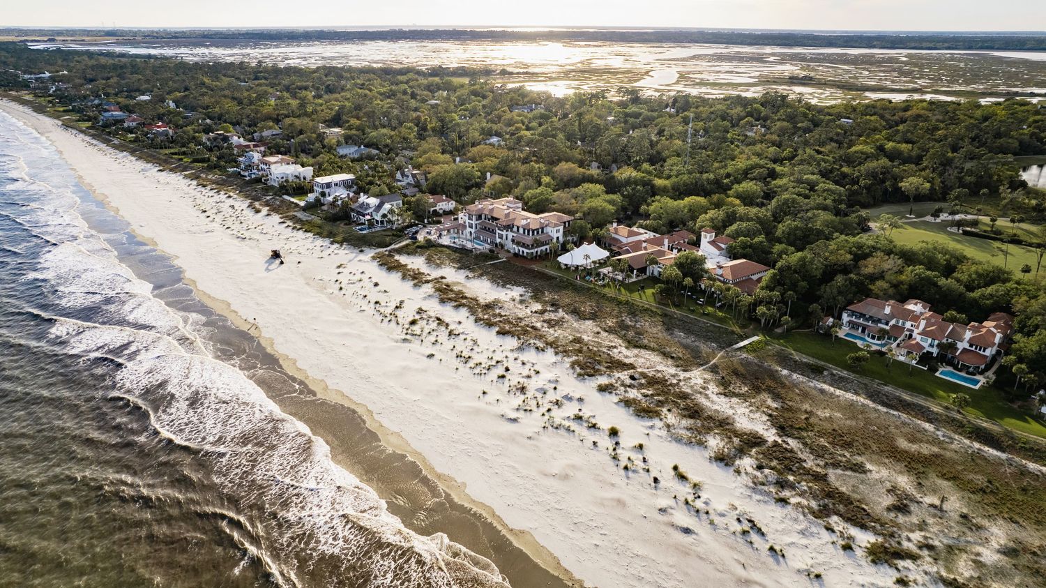 Aerial view of coastal homes along a sandy beach with rolling waves and lush vegetation on Kiawah Island, South Carolina.