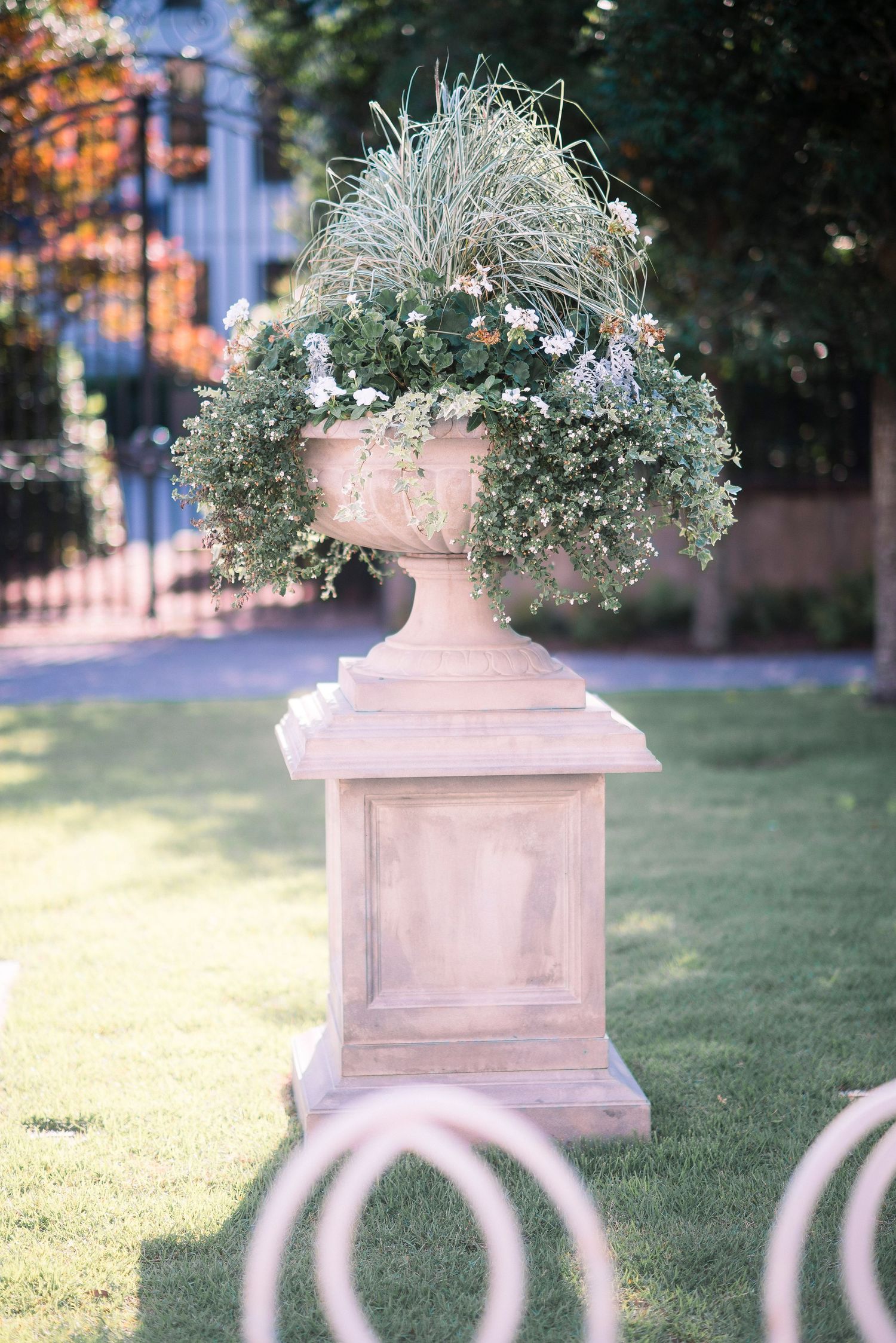 Decorative stone planters with overflowing greenery sit atop white fence posts in a garden setting at dusk.